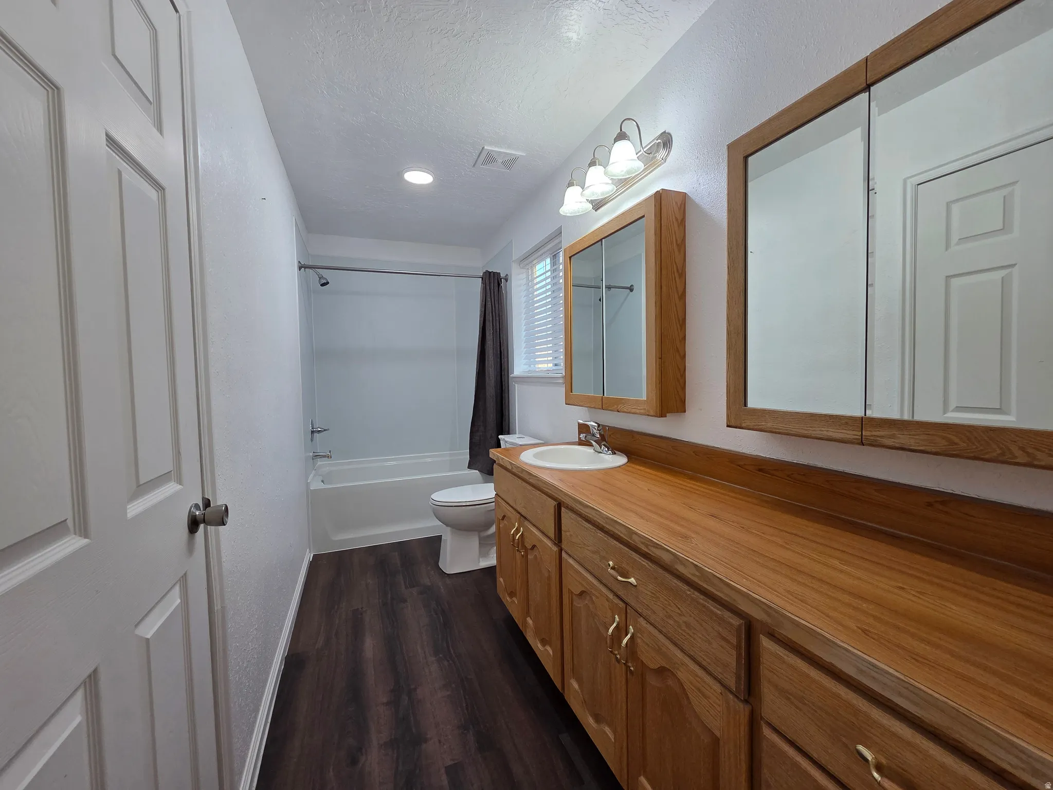Full bath with vanity, shower / bath combination with curtain, dark wood-style flooring, and a textured ceiling