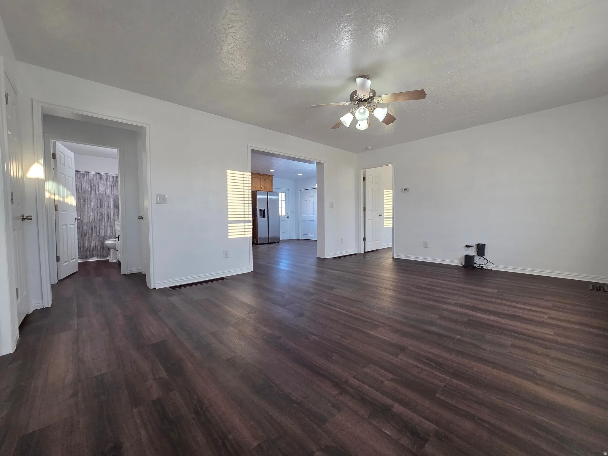 Unfurnished living room with dark wood finished floors, a textured ceiling, and a ceiling fan