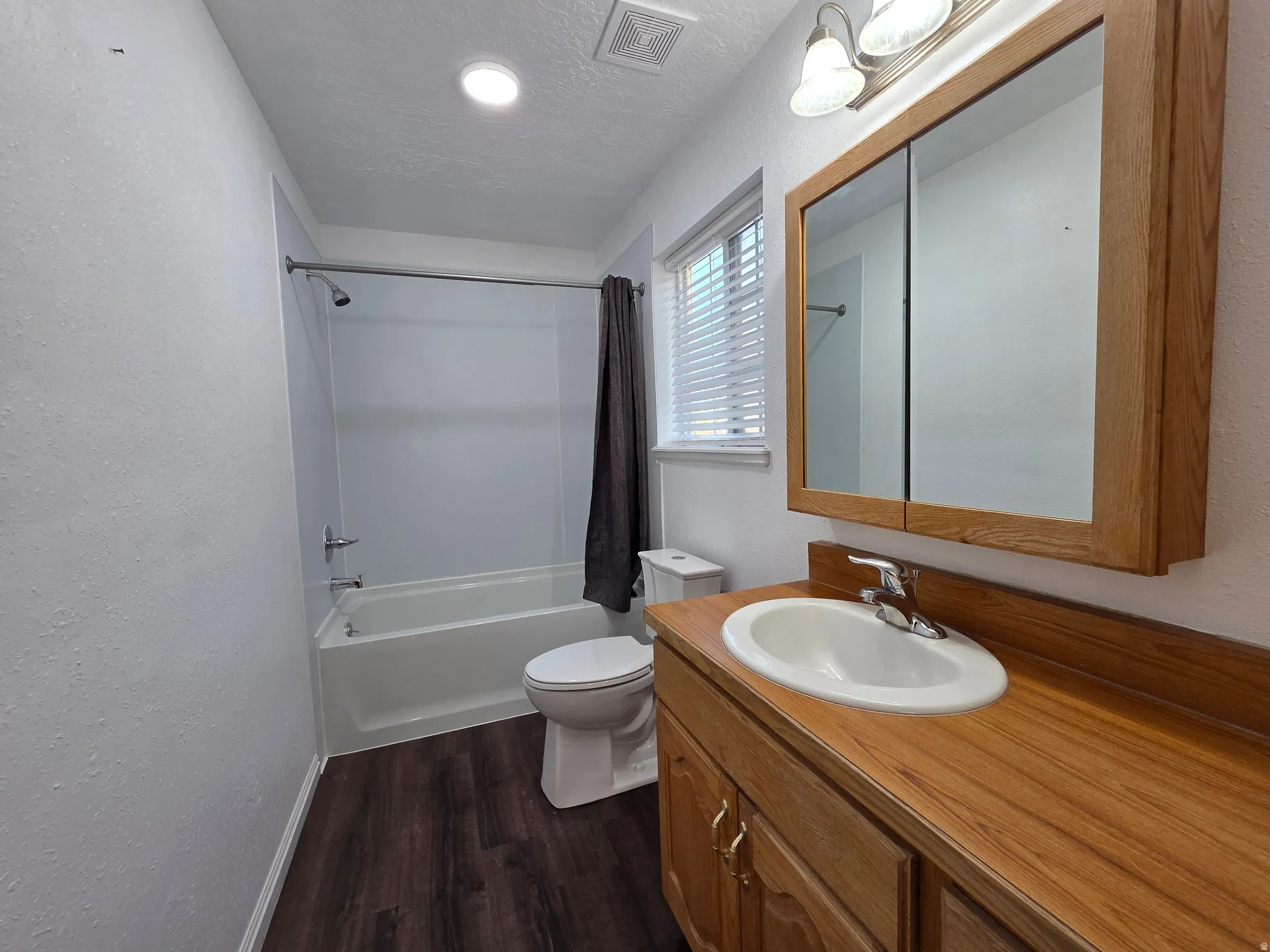 Bathroom with a textured wall, vanity, dark wood-style floors, shower / tub combo with curtain, and a textured ceiling