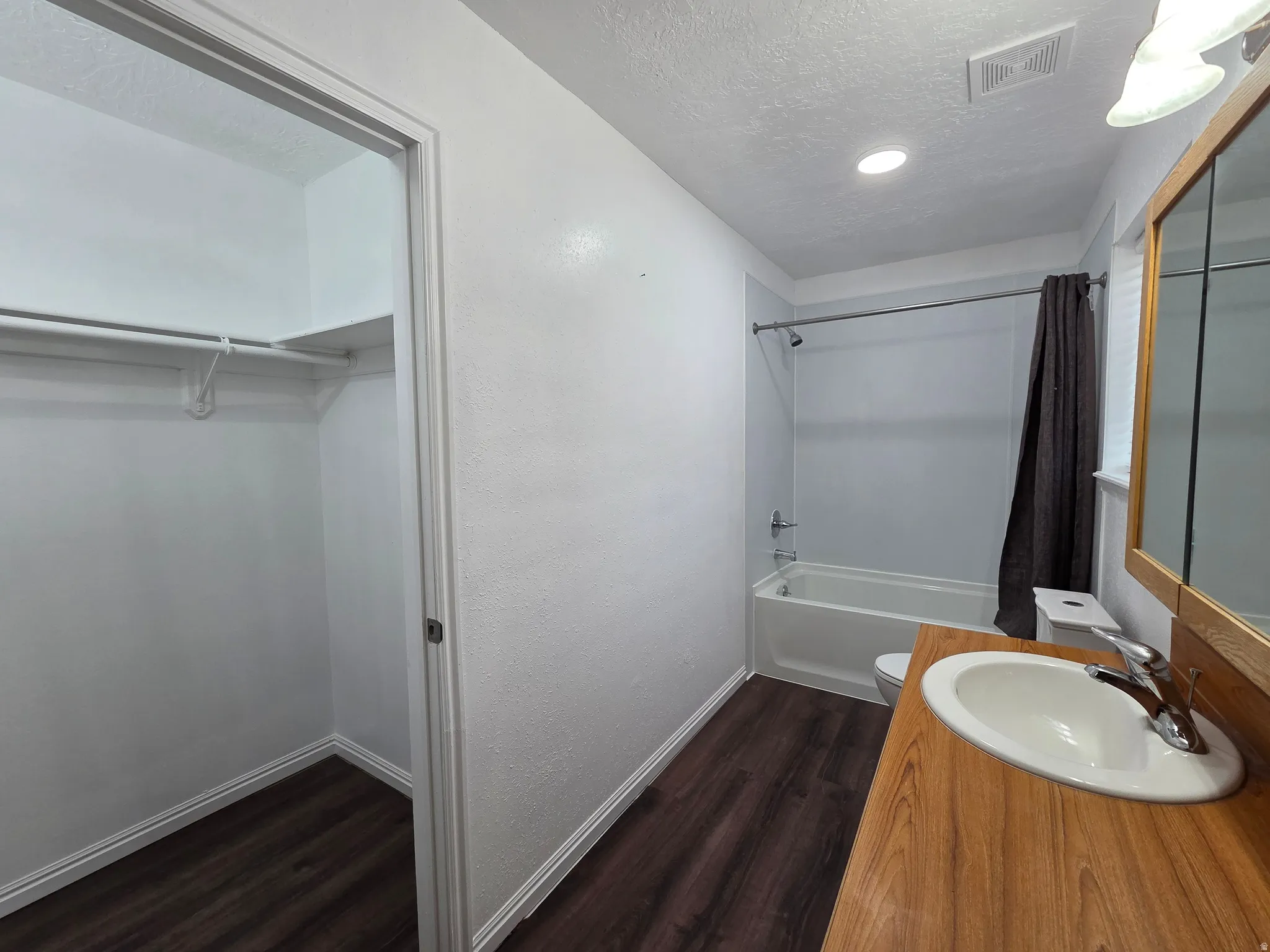 Full bath featuring dark wood-style floors, vanity, a textured ceiling, a walk in closet, and shower / tub combo with curtain