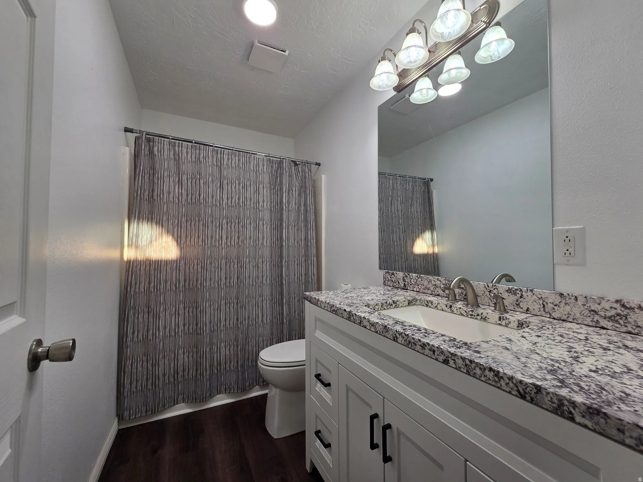 Full bath with vanity, curtained shower, dark wood-style floors, and a textured ceiling