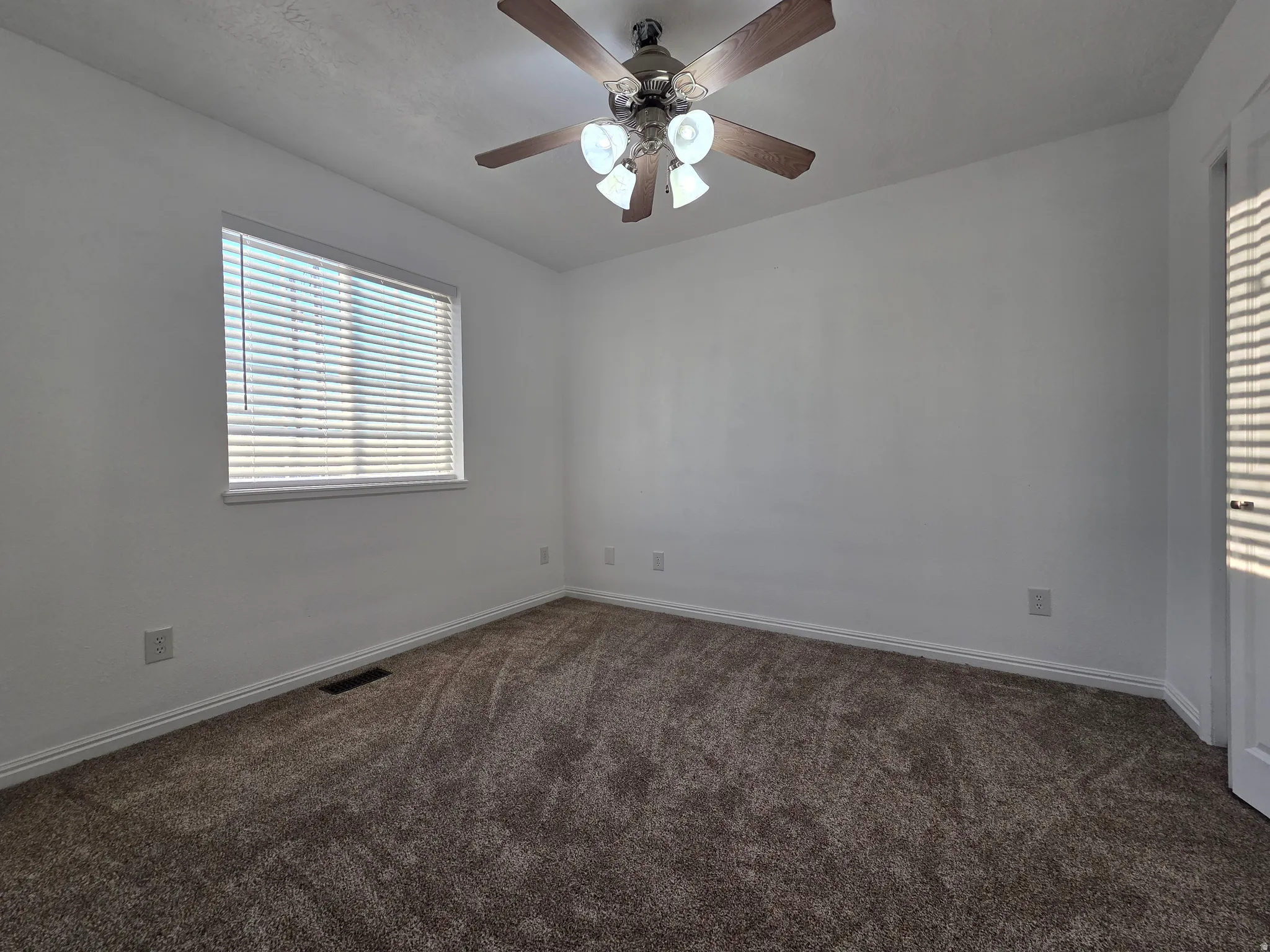 Empty room with dark carpet and a ceiling fan