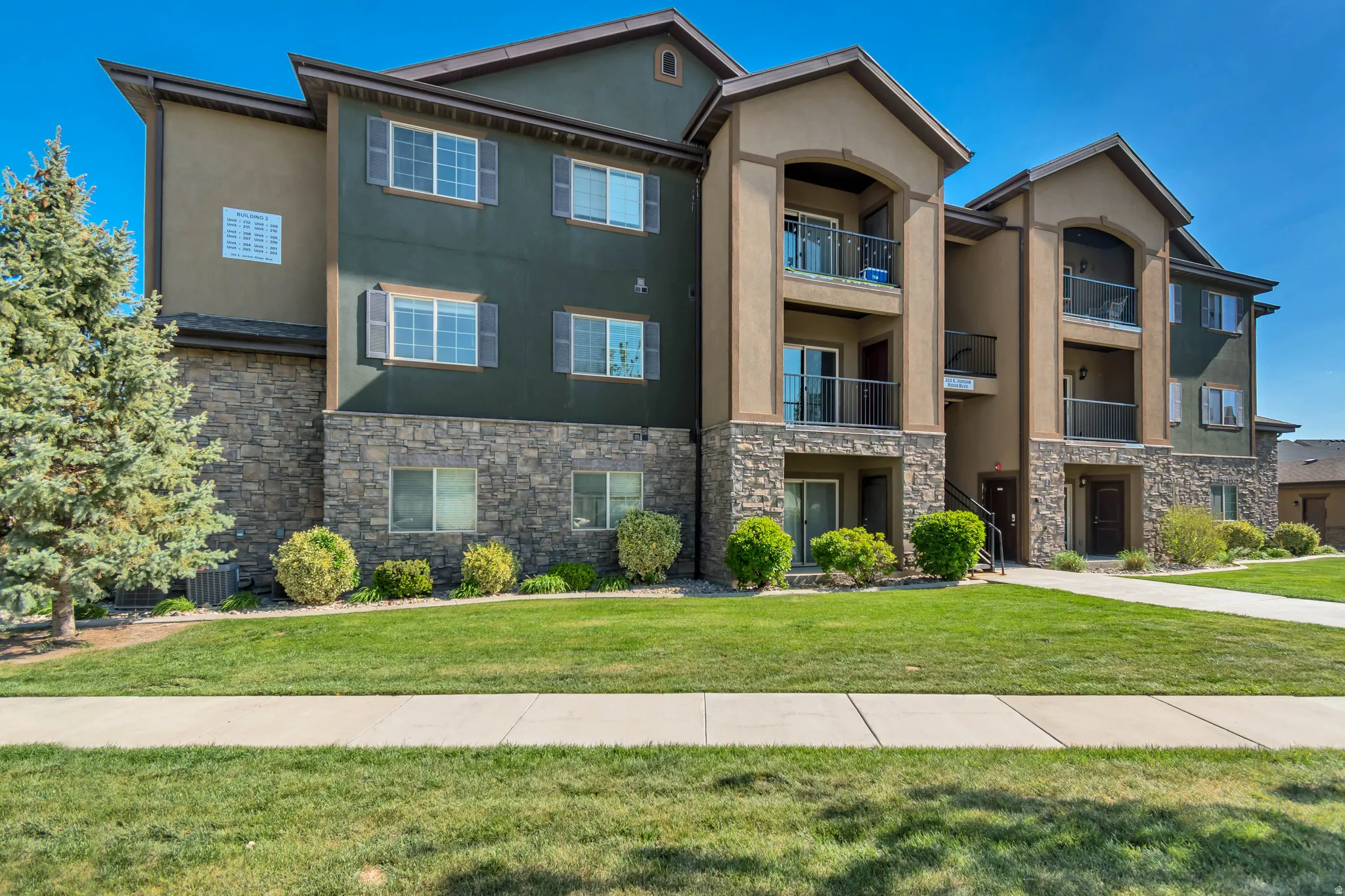 Multi-story building featuring a stone veneer base, stucco siding, individual balconies, and a manicured lawn