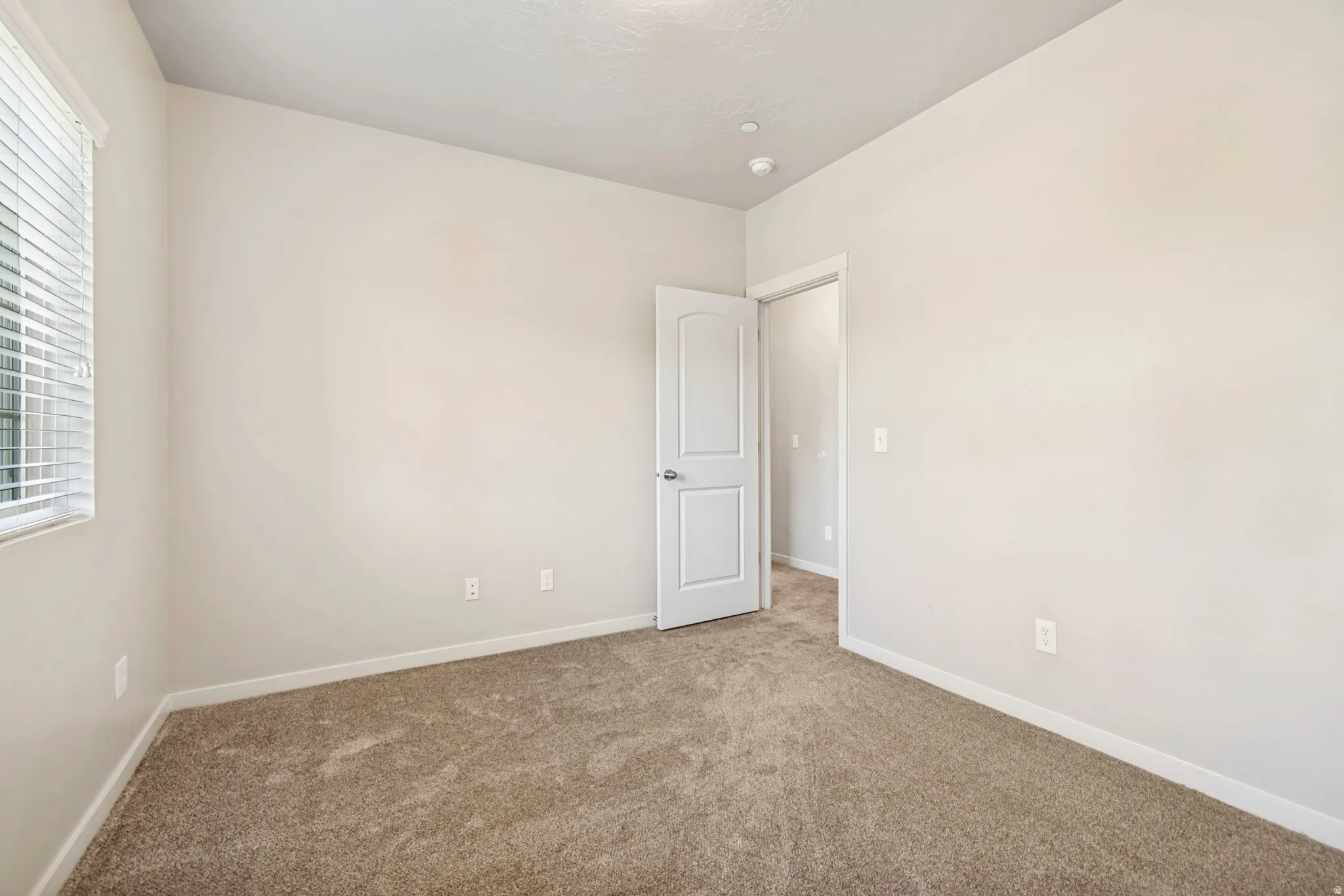 Neutral-toned room featuring light beige walls and a window with horizontal blinds