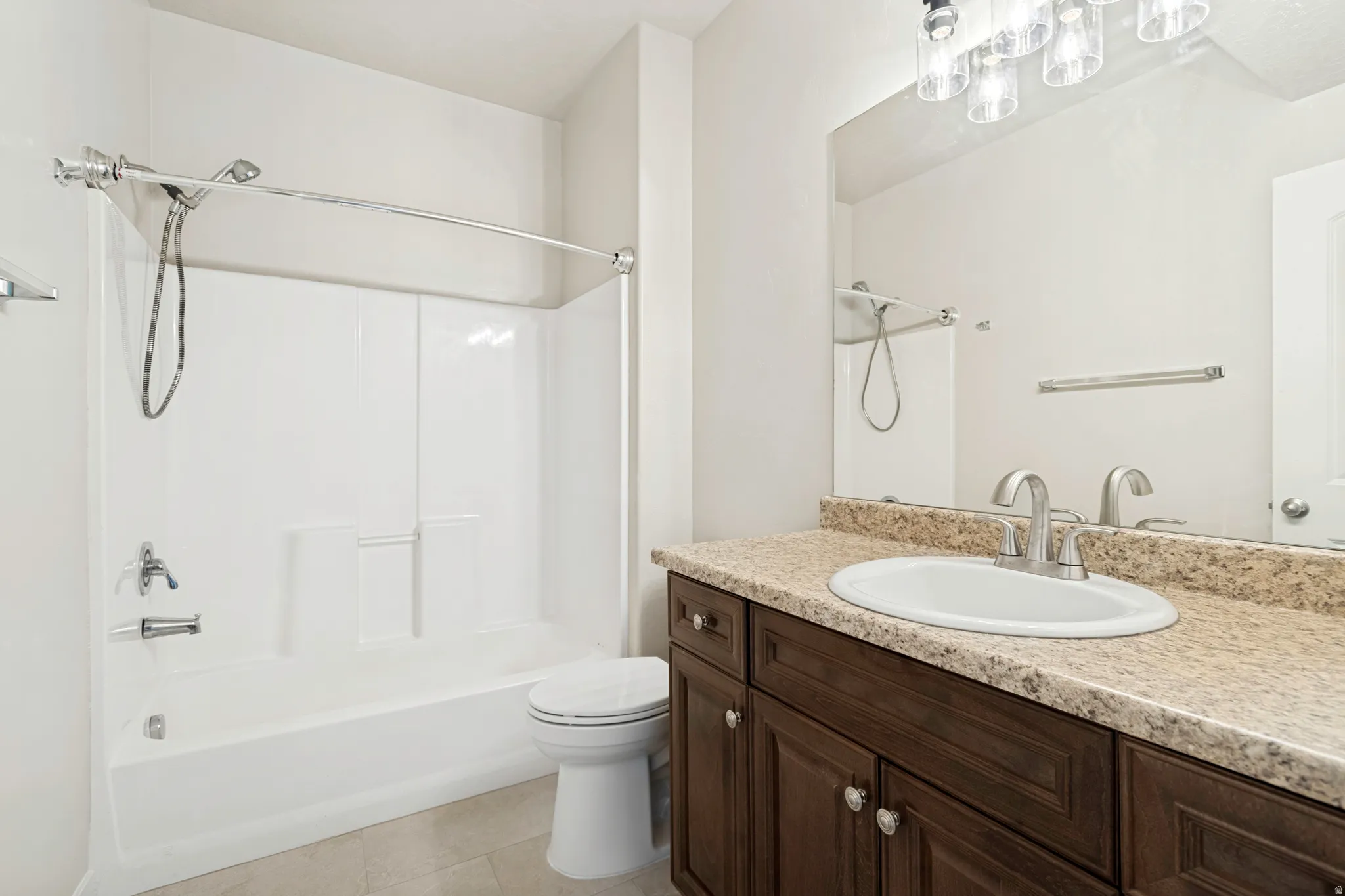 Bathroom featuring a white tub/shower combination, dark wood-finish vanity with an oval sink, speckled countertop, and a large wall-mounted mirror