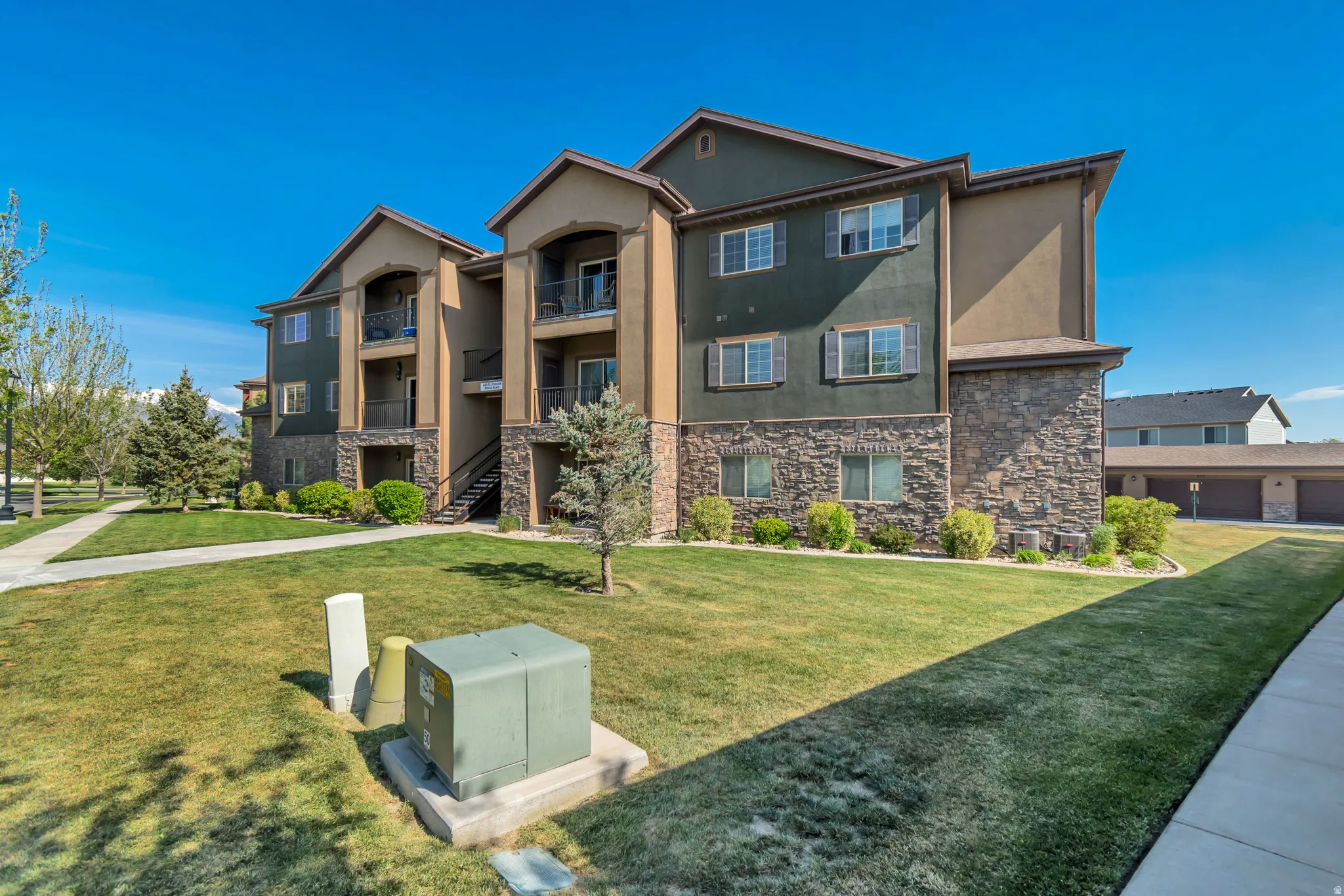 Multi-story residential building featuring balconies, stone veneer, and mature landscaping