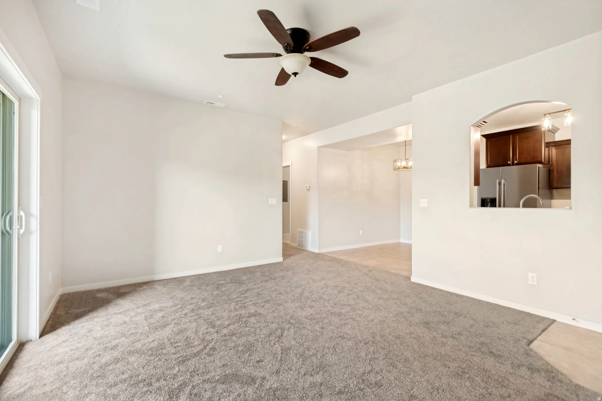 Spacious living area featuring neutral carpeting, a ceiling fan, and sliding glass door access