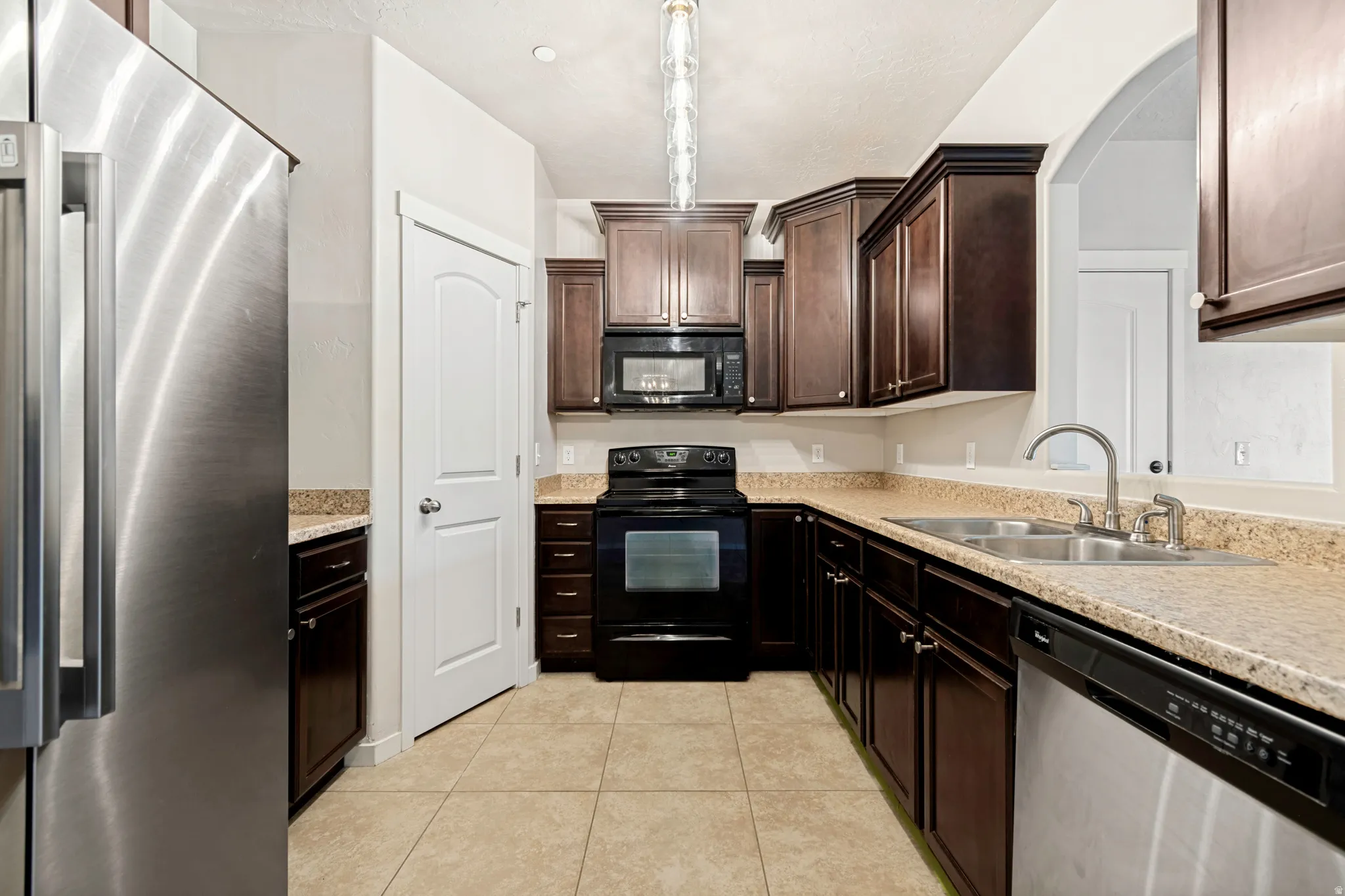 Kitchen featuring dark wood cabinetry, light speckled countertops, stainless steel refrigerator, black range, and black built-in microwave