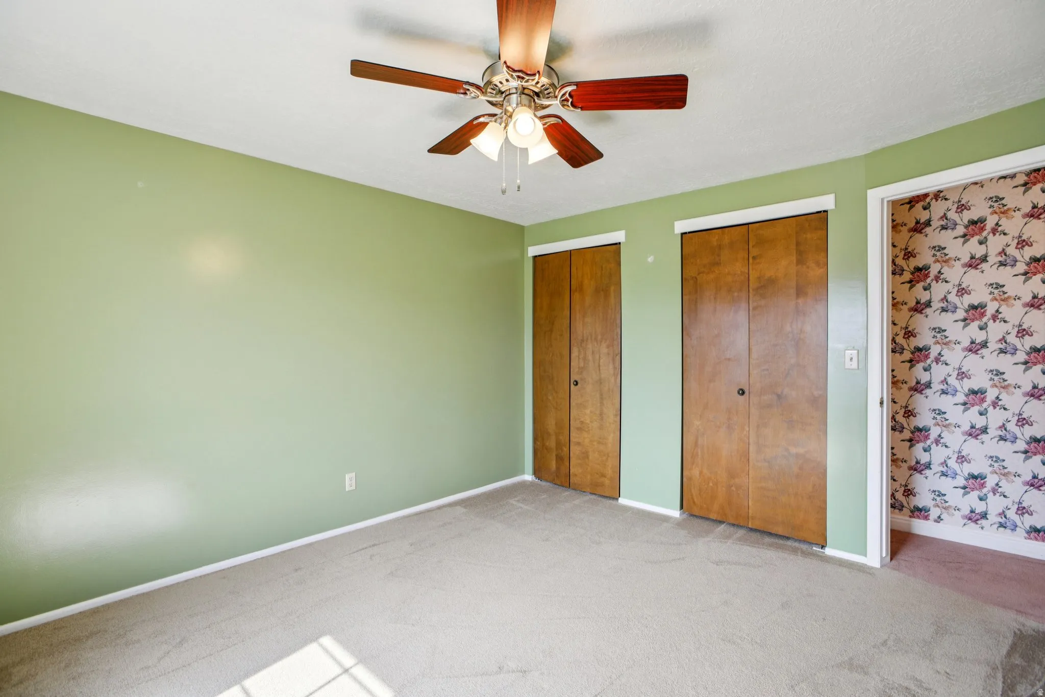 Unfurnished bedroom with two closets, light carpet, and ceiling fan