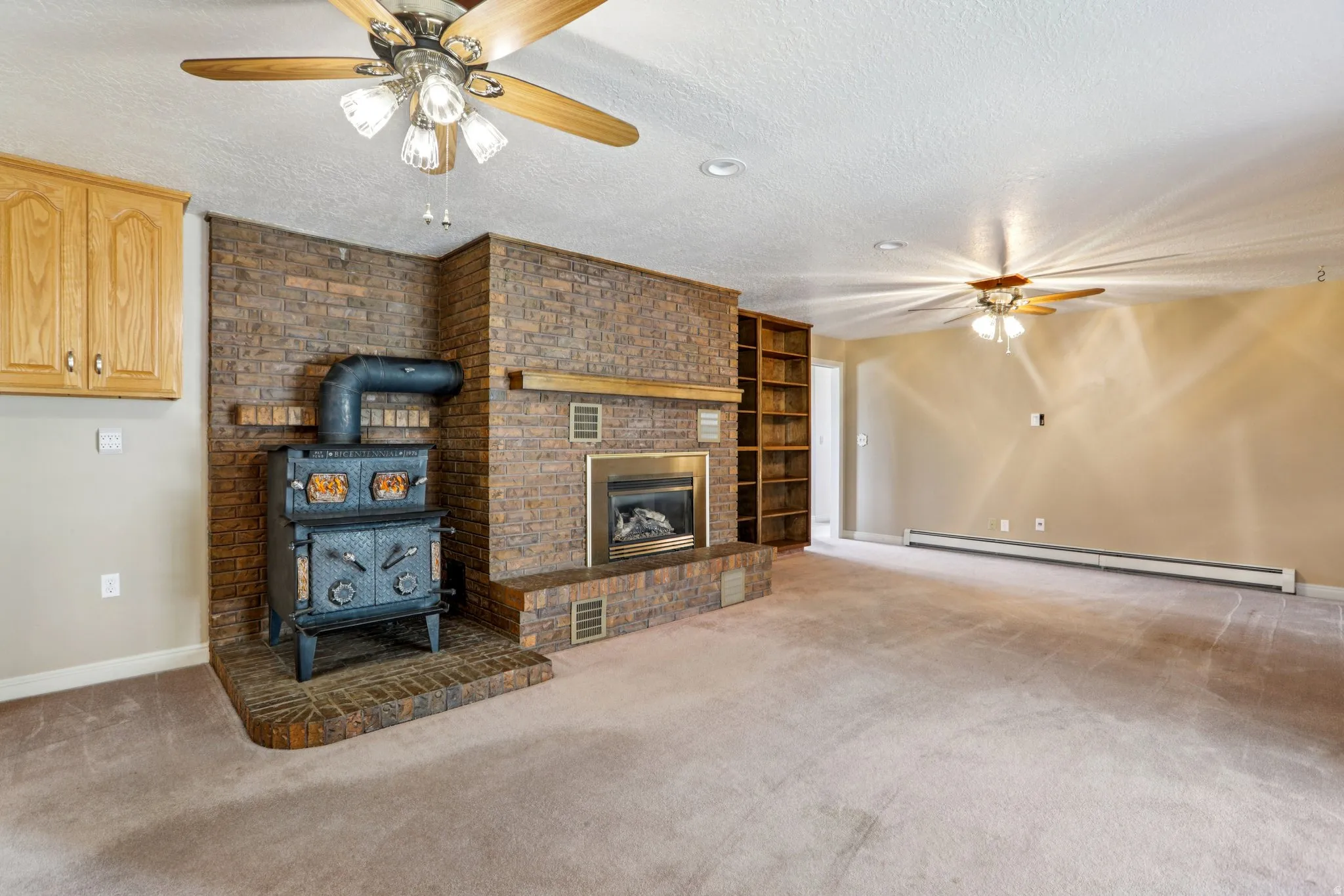 Unfurnished living room with a ceiling fan, a baseboard heating unit, a textured ceiling, carpet, and a wood stove