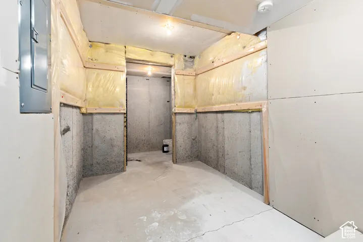 Unfinished lower level with exposed concrete walls, partially framed and insulated walls, and a circuit breaker panel