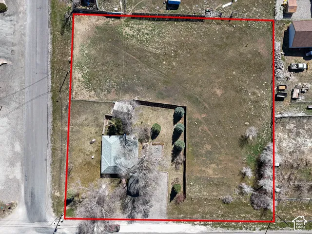 Aerial view of a rectangular lot featuring an expansive open yard, perimeter fencing, mature trees, and direct road access