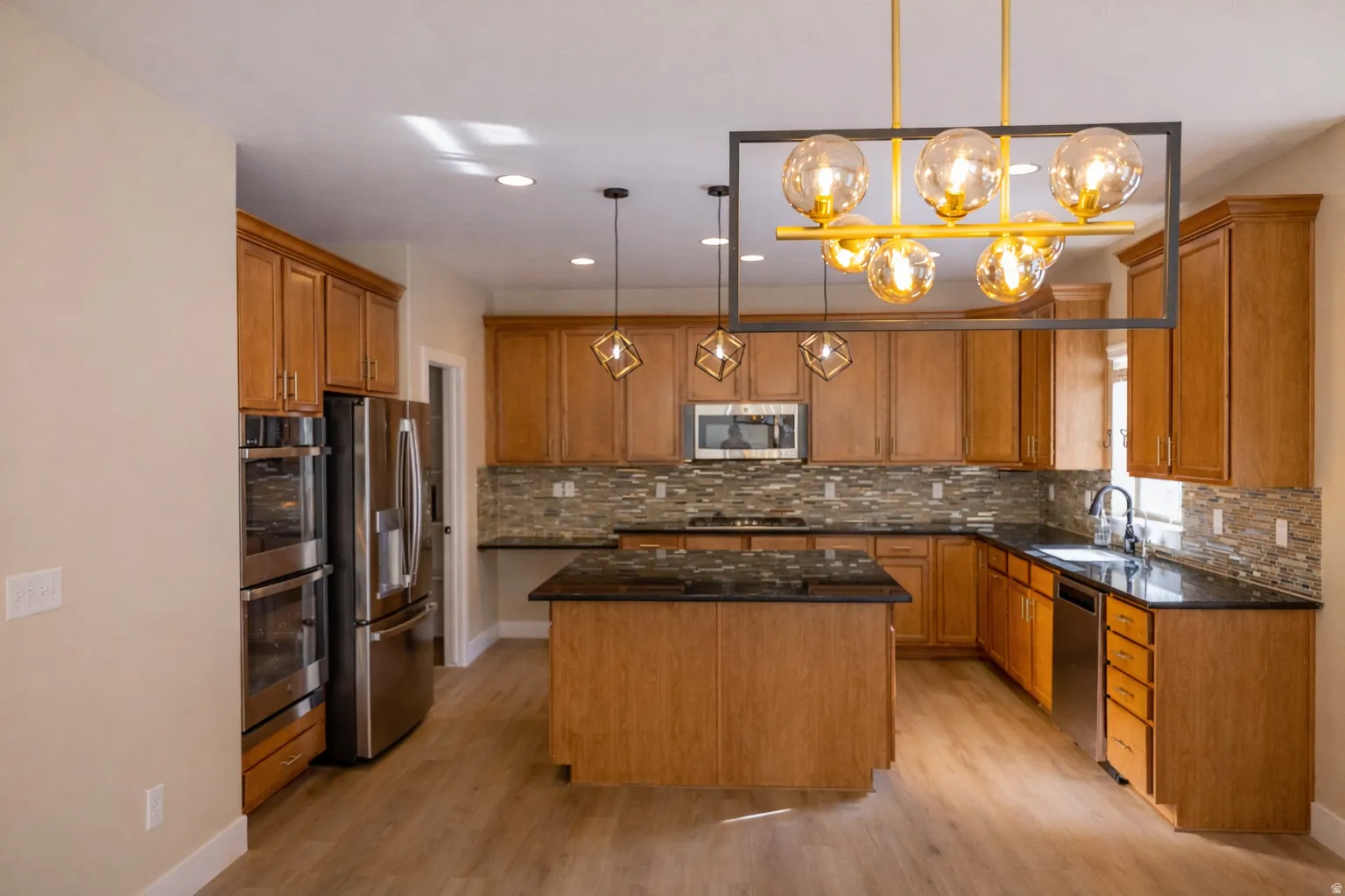 Kitchen with a center island, dark stone counters, wood finish cabinetry, stainless steel appliances, and hanging light fixtures