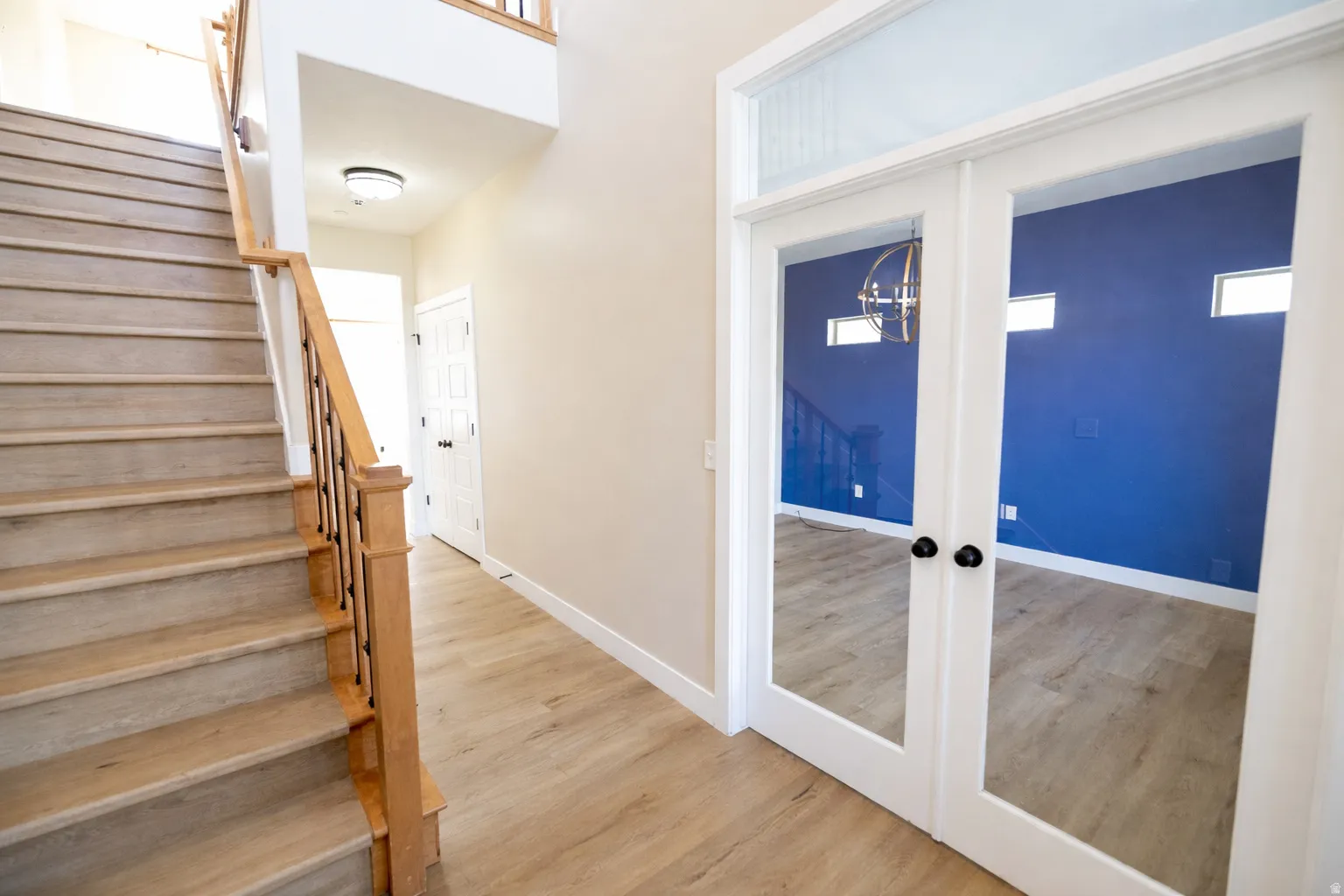 Bright entryway with staircase, wood railing, brand-new LVP waterproof flooring, and French doors opening to a private office or den