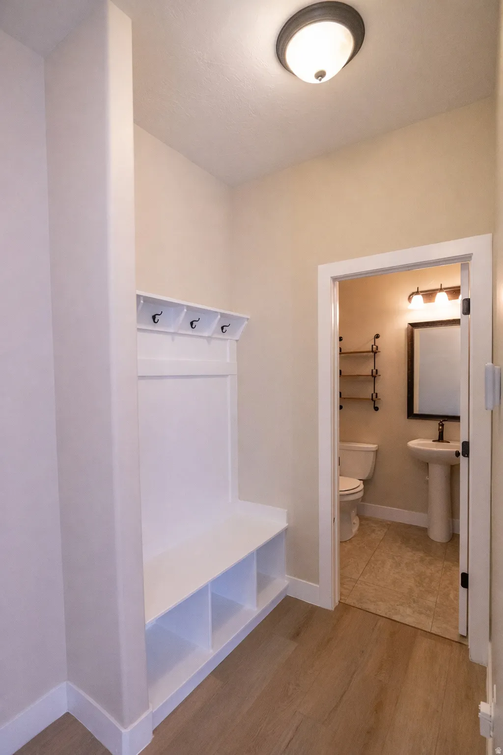 Newly painted mudroom featuring a built-in bench with coat hooks and storage cubbies, located next to the main-level powder bath, kitchen and garage