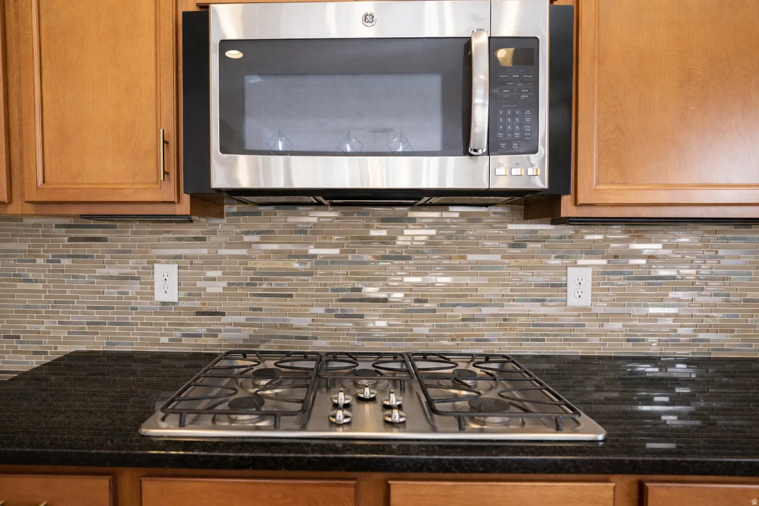 Kitchen with stainless steel appliances, dark stone countertops, wood finish cabinetry, and tasteful backsplash