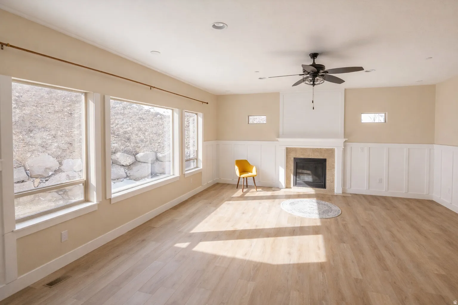 Unfurnished living room with a wainscoted wall, a ceiling fan, light wood-type flooring, a decorative wall, and a tiled fireplace