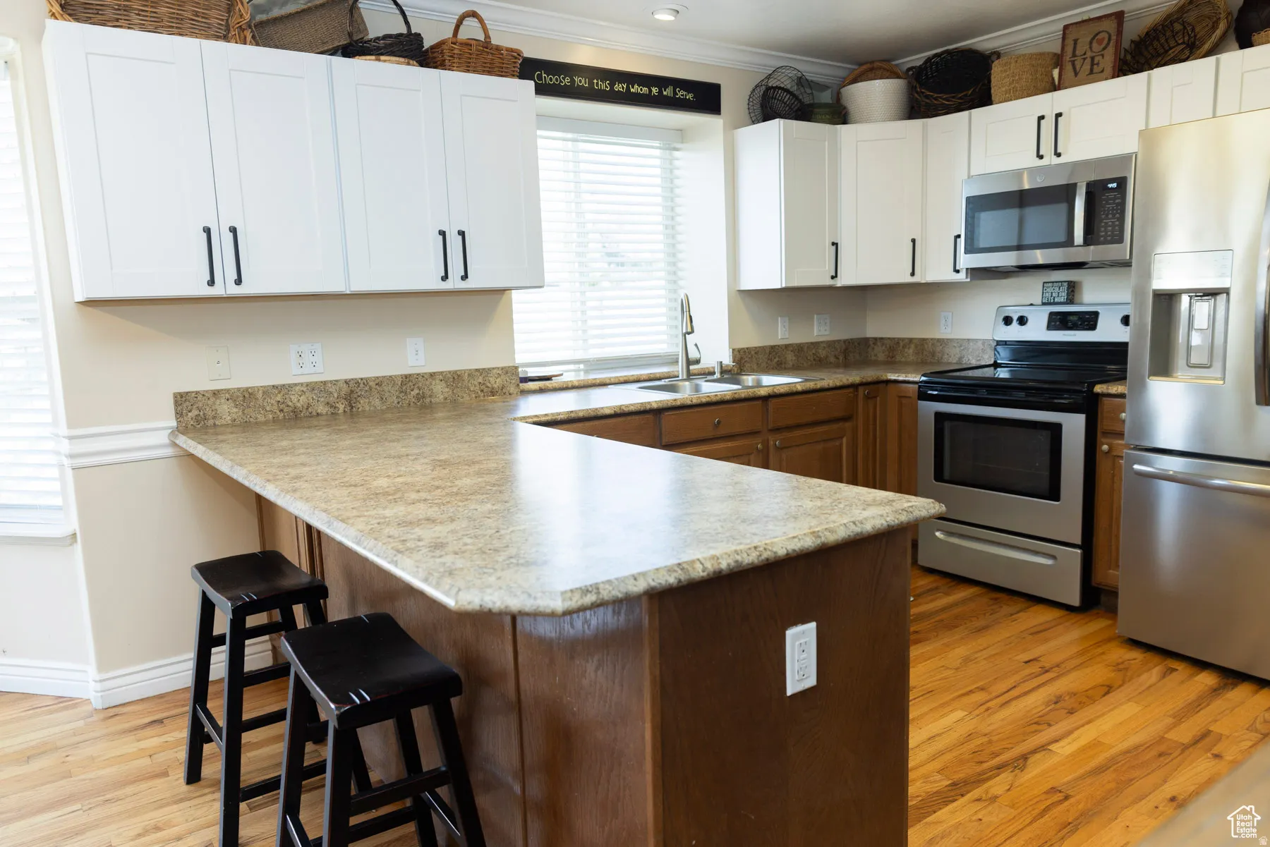 Kitchen featuring a peninsula, a kitchen bar, stainless steel appliances, light wood-style flooring, and crown molding