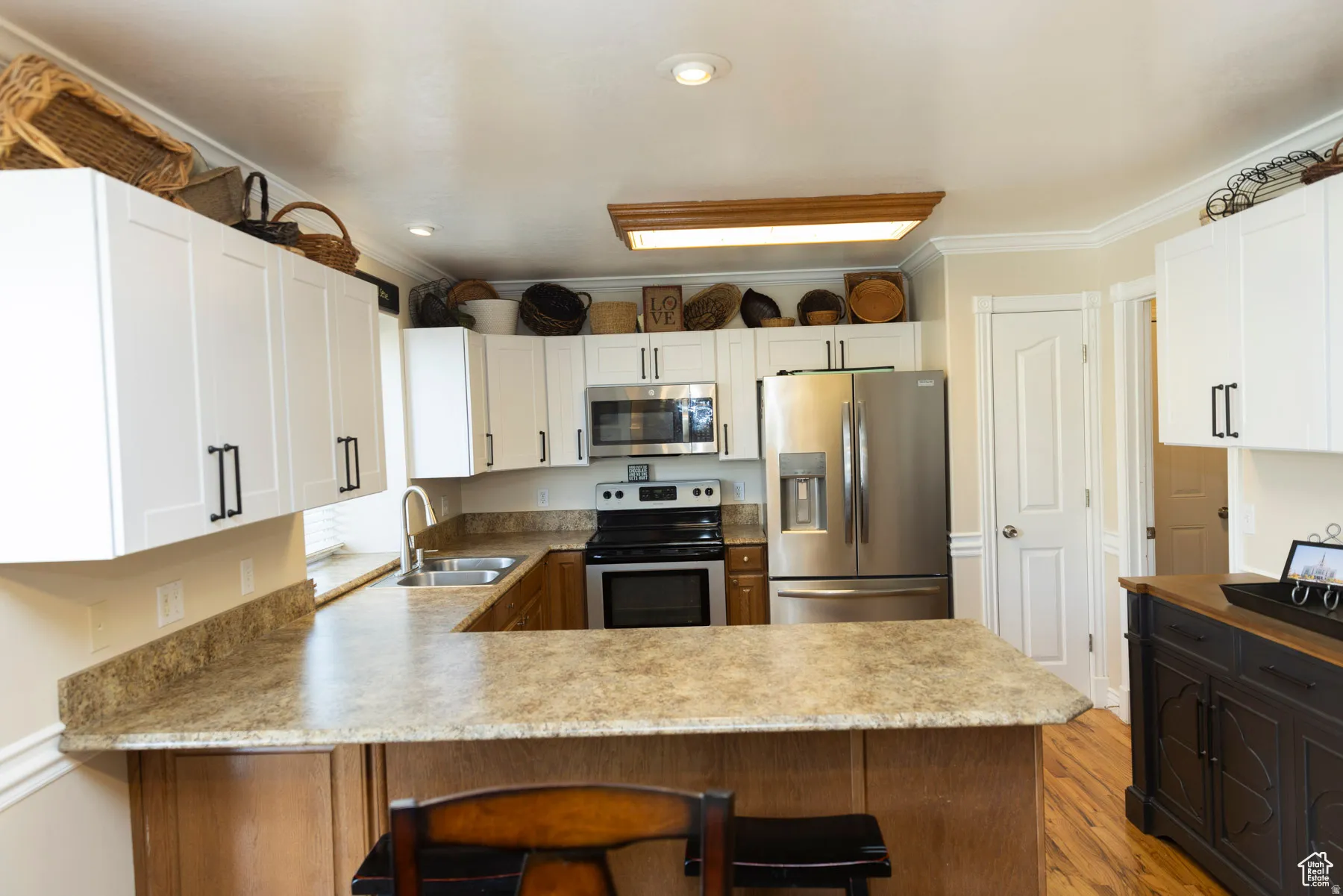 Kitchen featuring stainless steel appliances, a peninsula, a kitchen breakfast bar, crown molding, and light wood-style floors