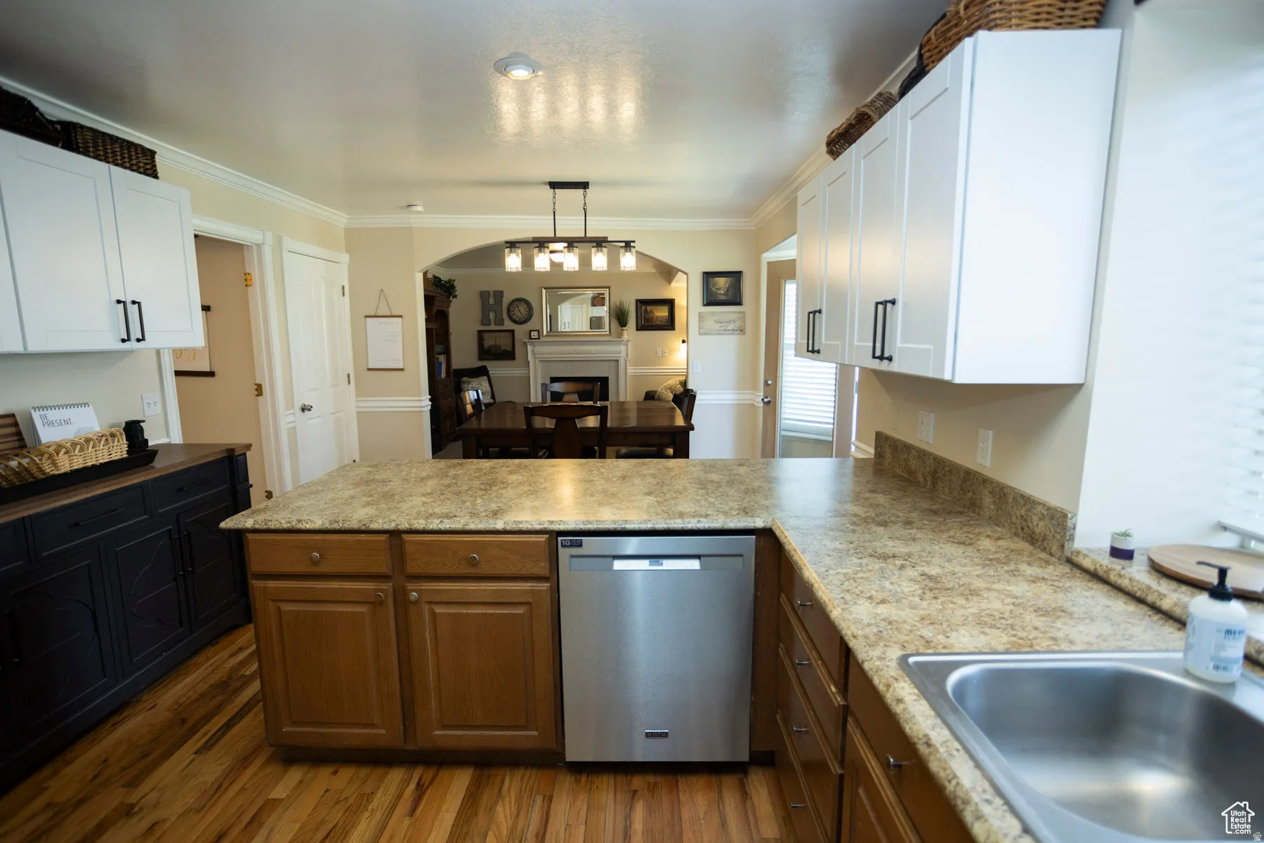Kitchen featuring dishwasher, a fireplace, a peninsula, crown molding, and light countertops