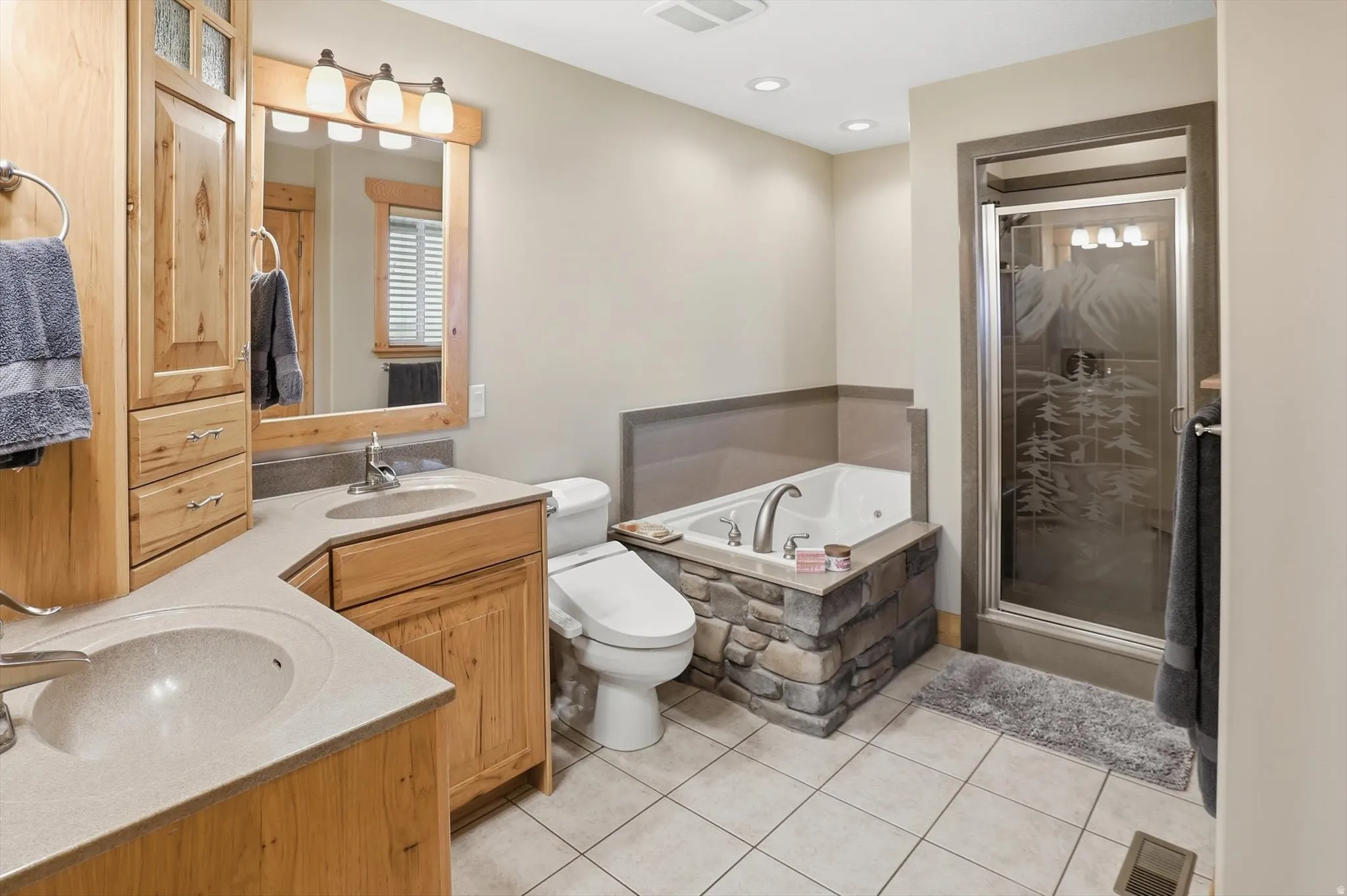 Primary bathroom ensuite with full bath, double vanity, a bath, a stall shower, light tile patterned floors, and recessed lighting