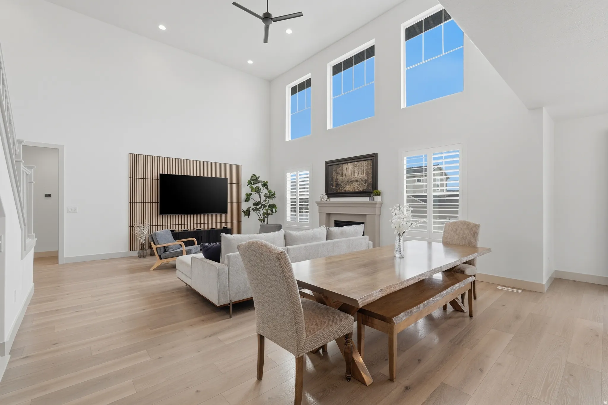 Dining room featuring light wood-style floors, a high ceiling, a fireplace, ceiling fan, and recessed lighting