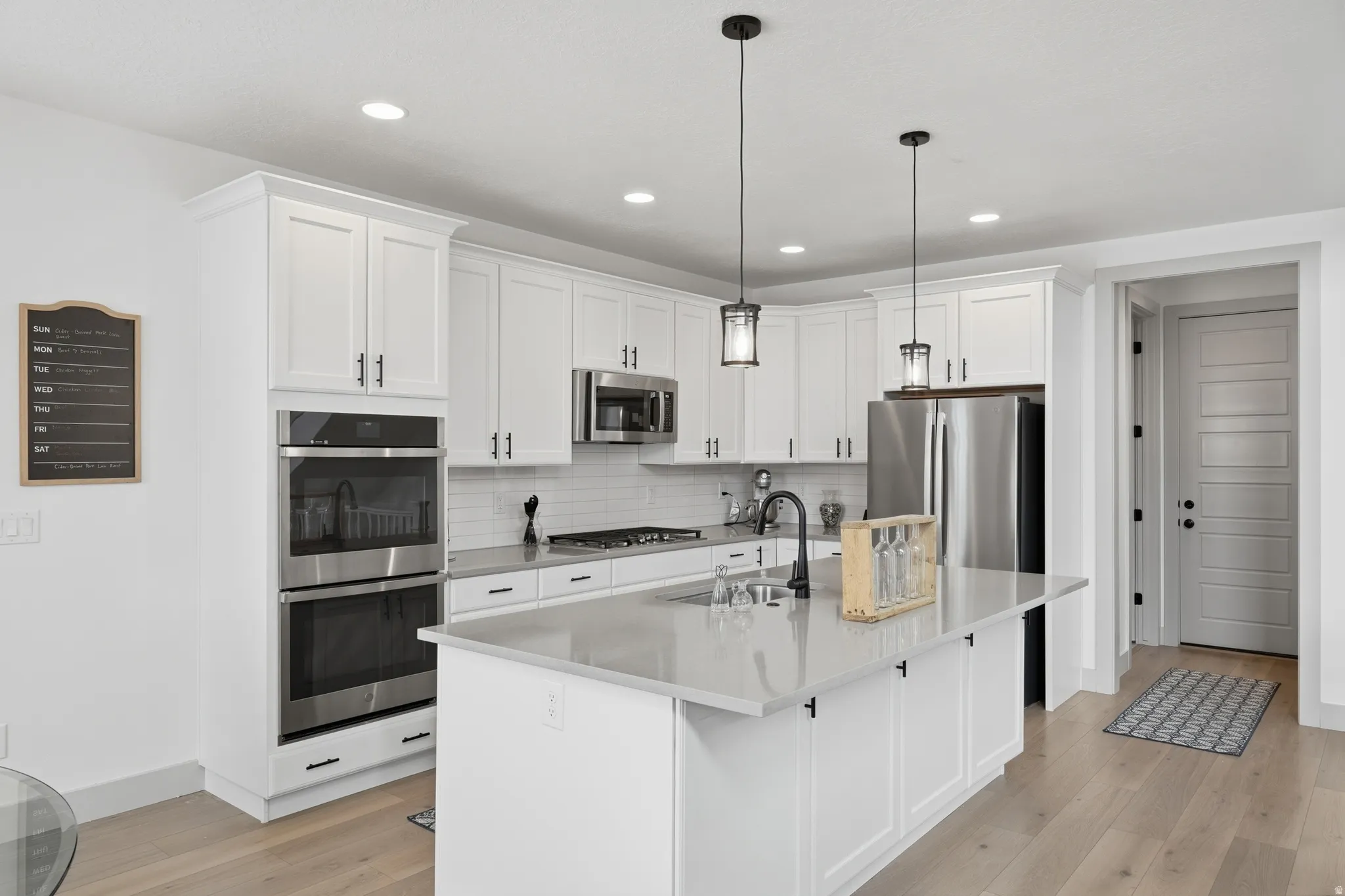Kitchen with white cabinets, stainless steel appliances, an island with sink, light wood-style flooring, and tasteful backsplash