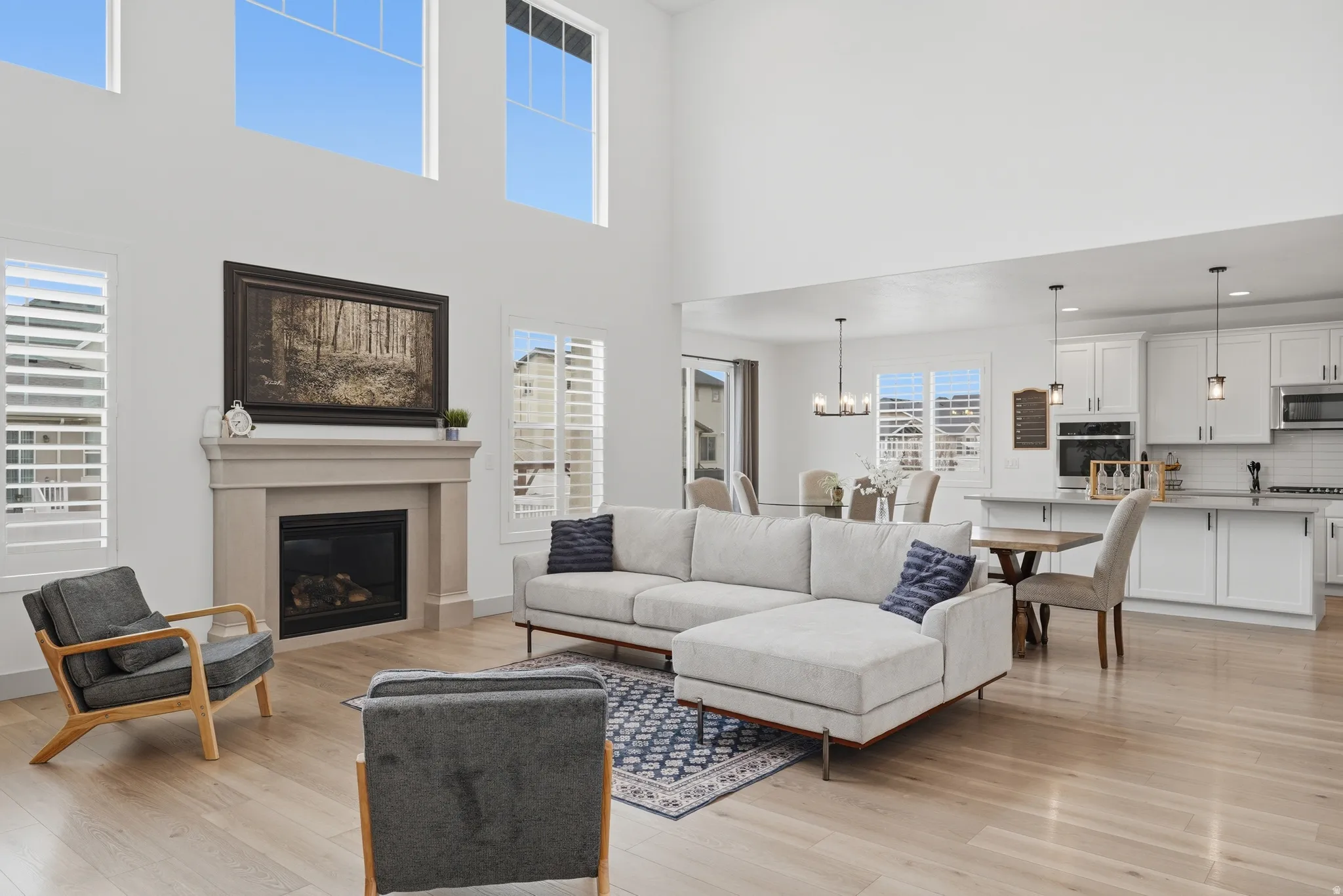 Living area featuring light wood-style floors, a glass covered fireplace, a high ceiling, and suspended lighting