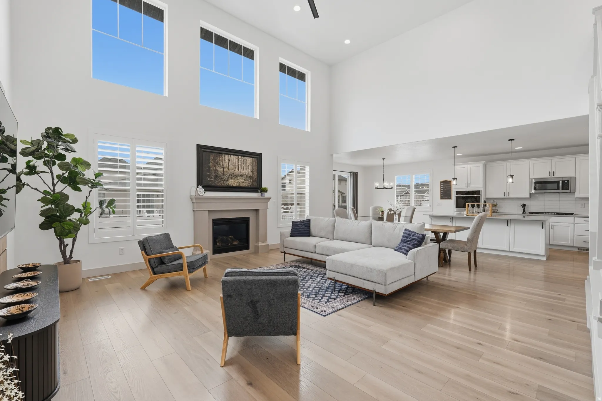 Living room featuring a glass covered fireplace, light wood-style floors, a high ceiling, suspended lighting, and ceiling fan