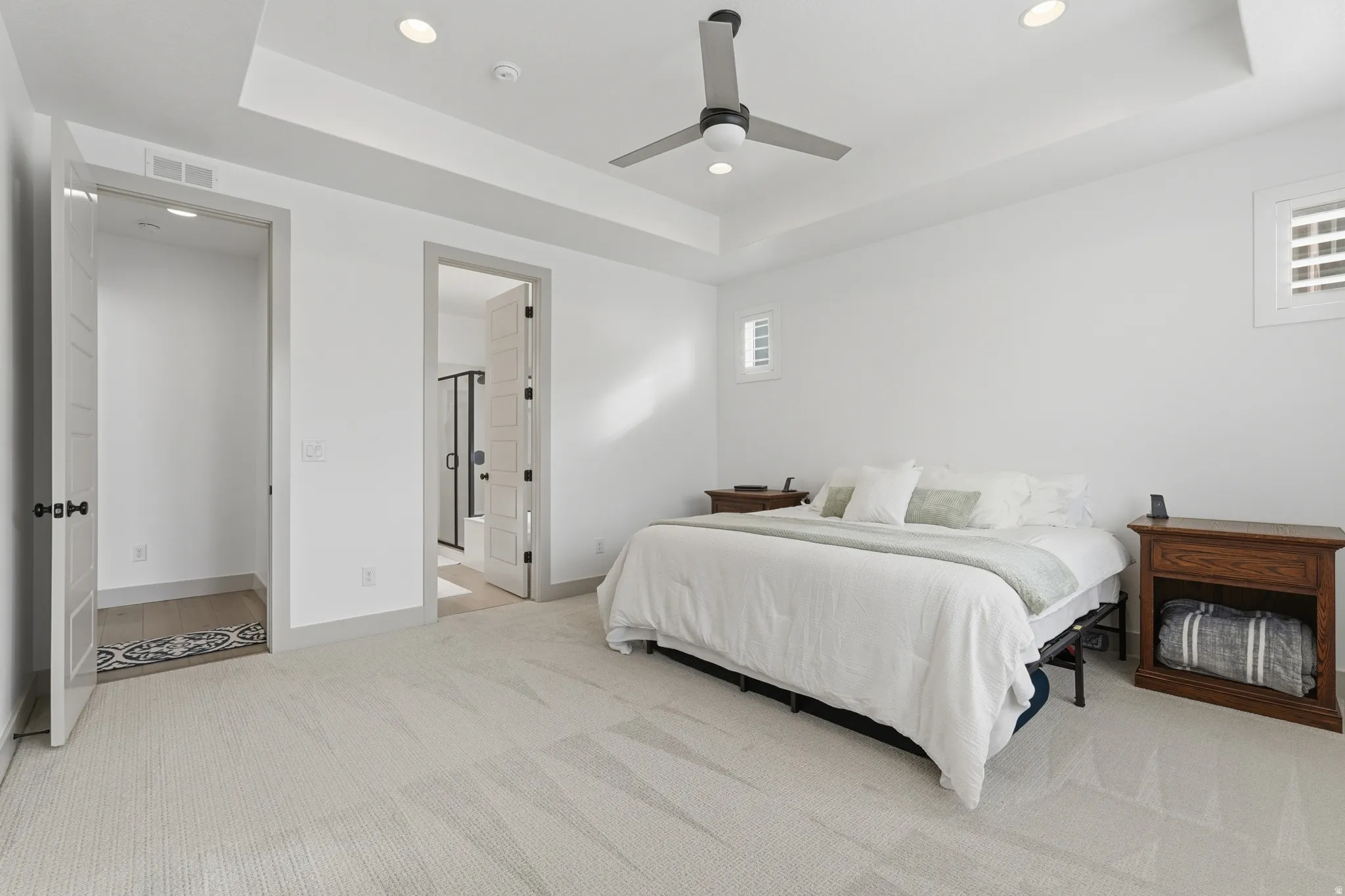 Bedroom with a tray ceiling, recessed lighting, light colored carpet, ceiling fan, and ensuite bath