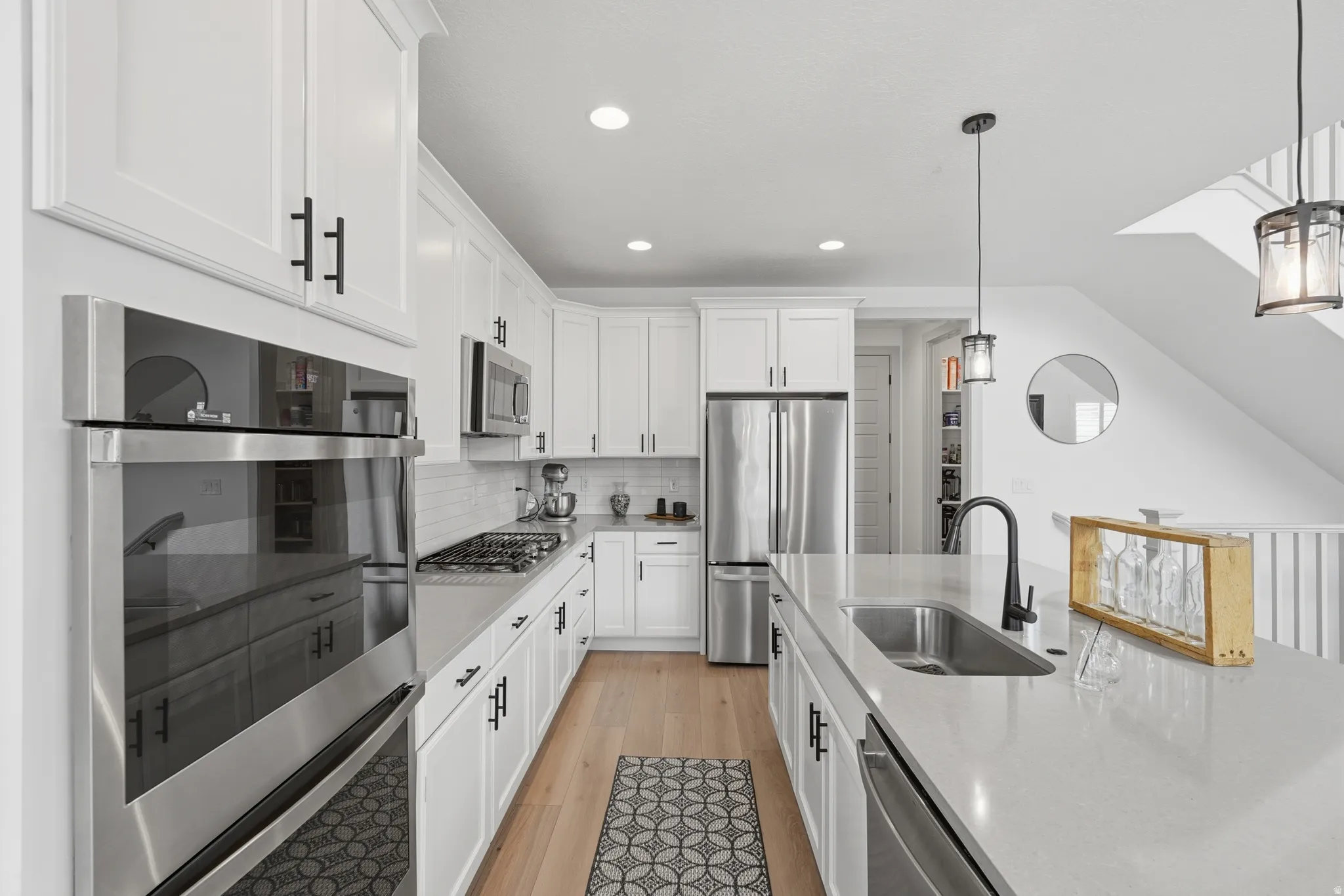 Kitchen with white cabinetry, stainless steel appliances, backsplash, and hanging light fixtures