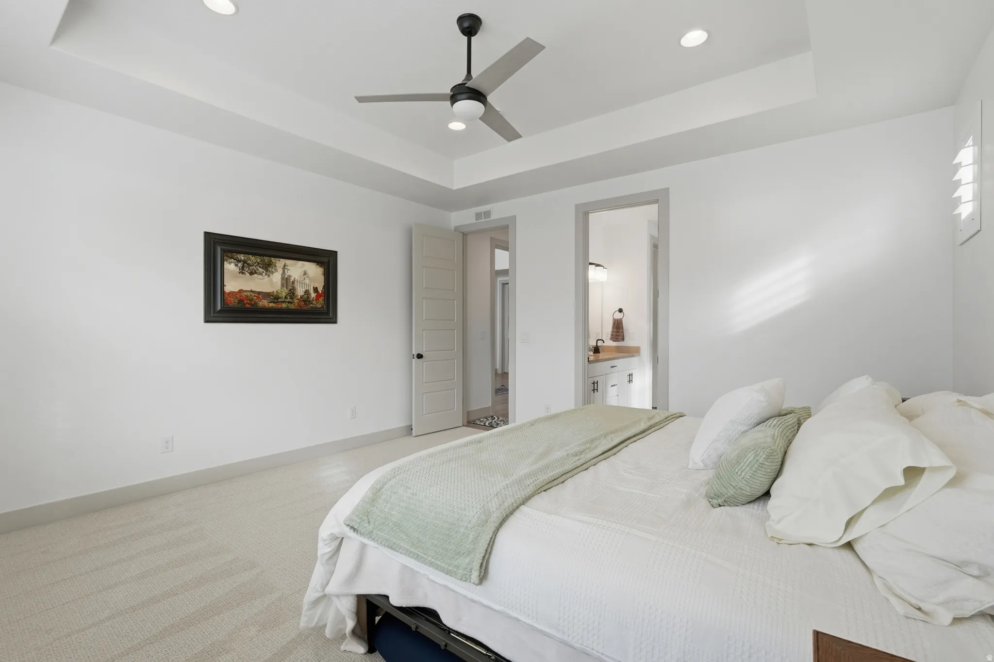 Bedroom with a raised ceiling, carpet flooring, recessed lighting, ceiling fan, and connected bathroom