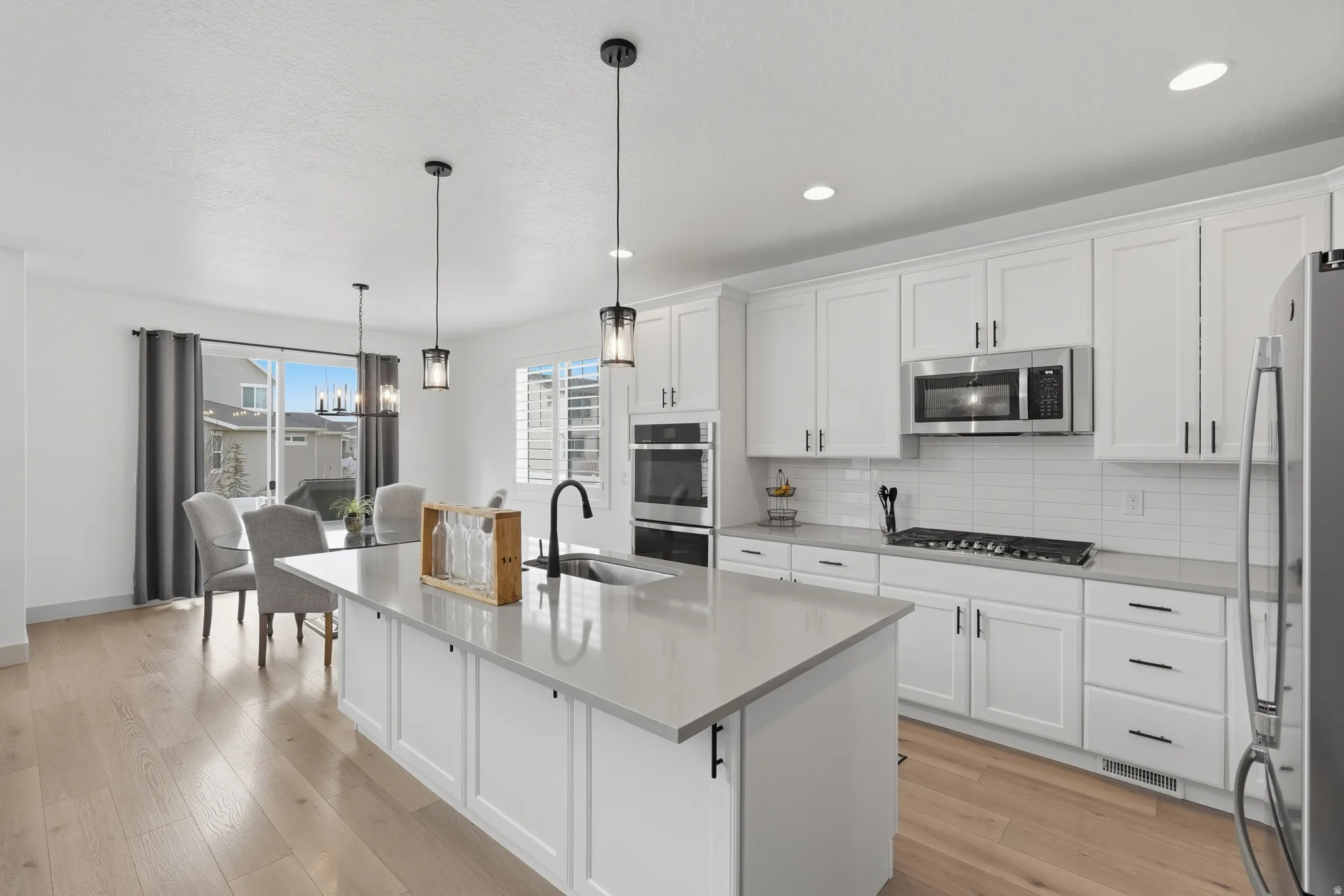Kitchen featuring white cabinetry, backsplash, a center island with sink, and stainless steel appliances