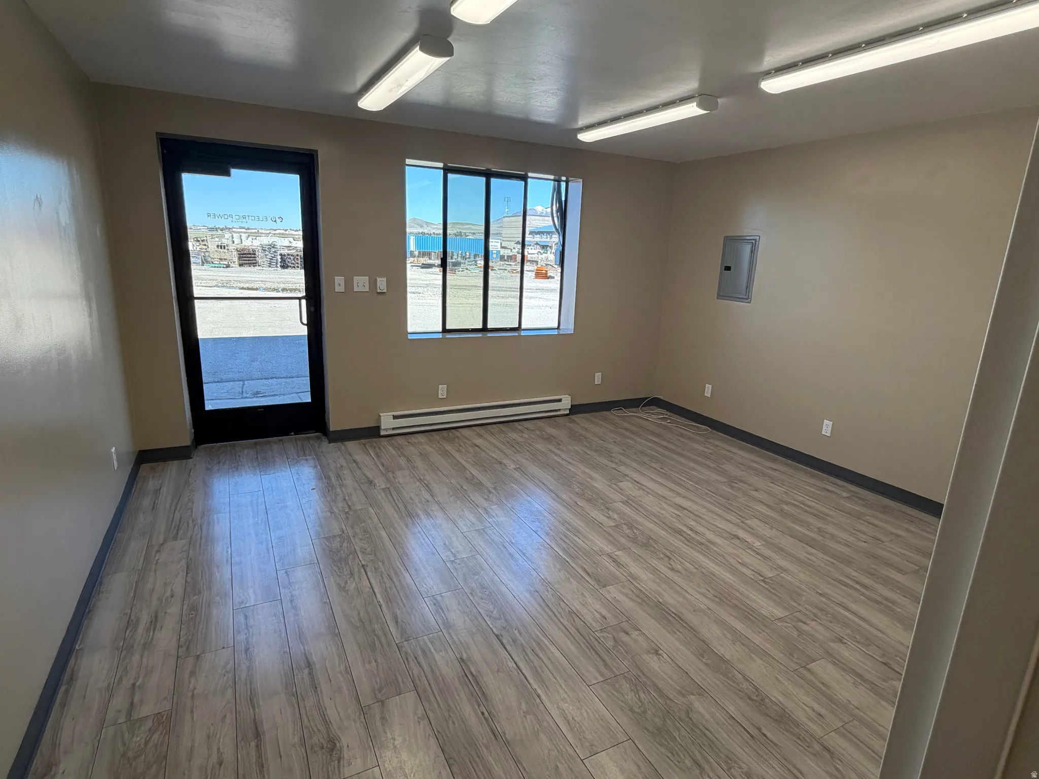 Unfurnished room featuring wood finished floors, a baseboard radiator, and electric panel