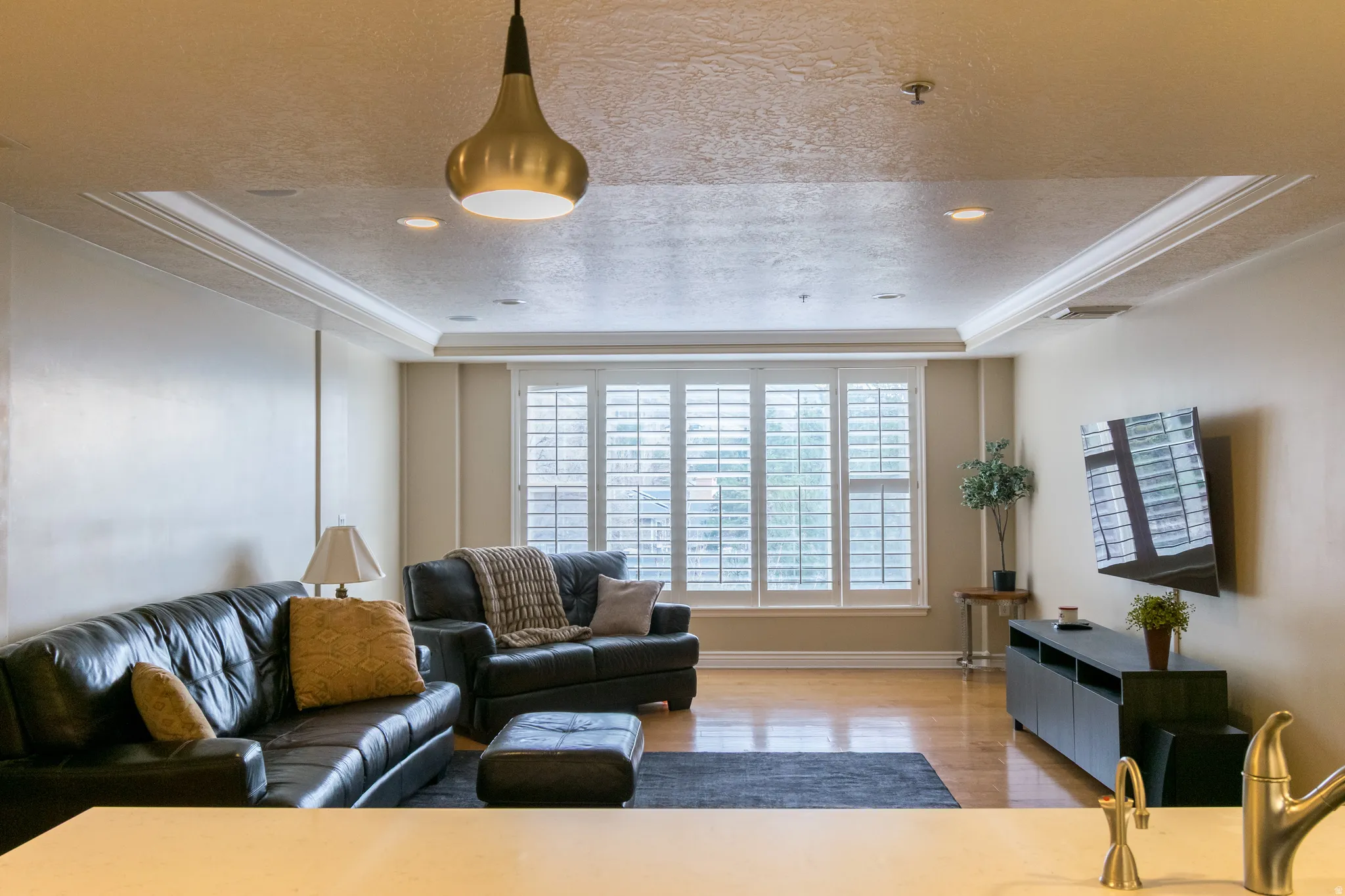 Living area featuring a raised ceiling, a textured ceiling, light wood-style flooring, crown molding, and recessed lighting