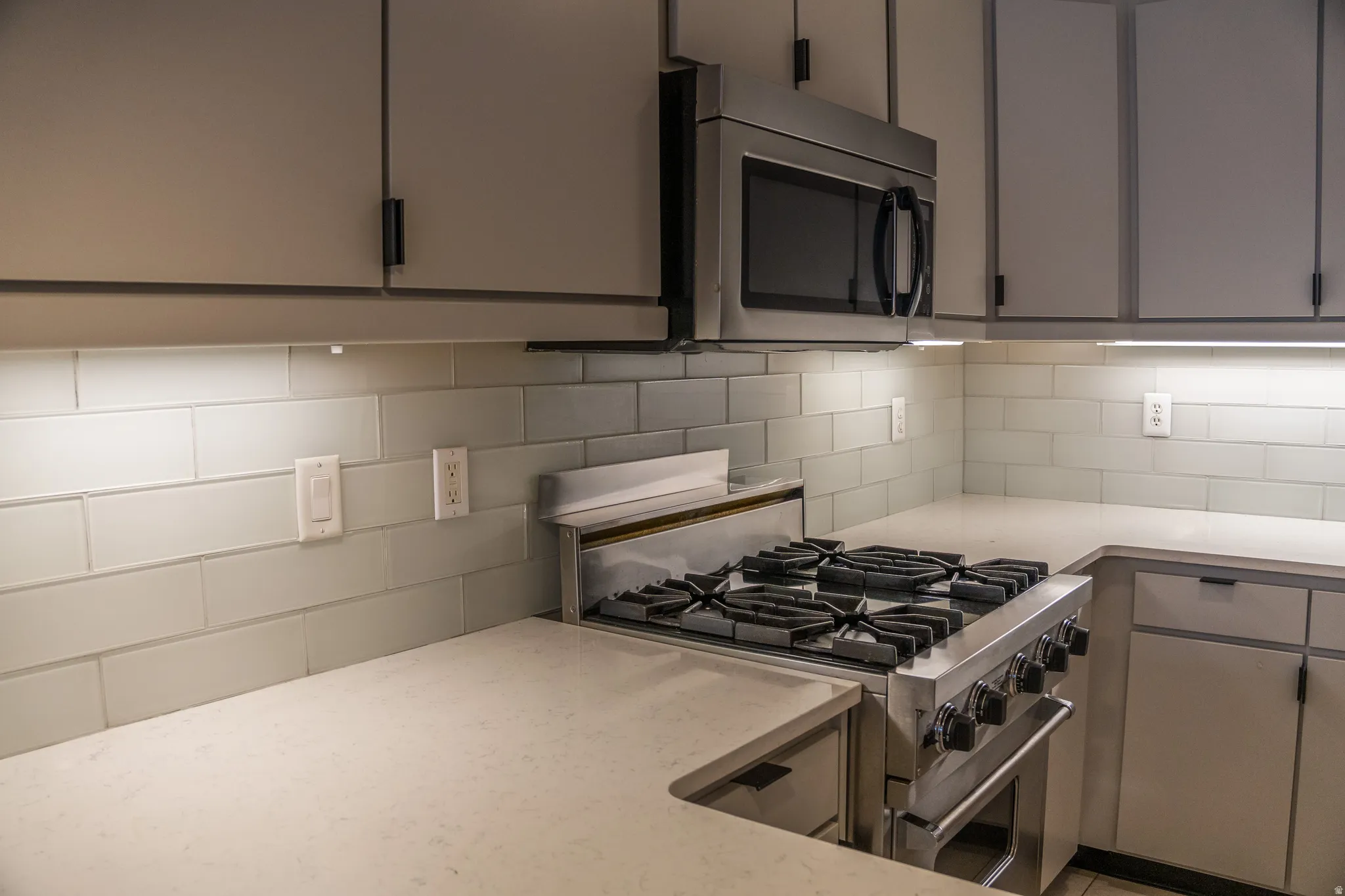 Kitchen with gray cabinetry, stainless steel appliances, backsplash, and light stone countertops