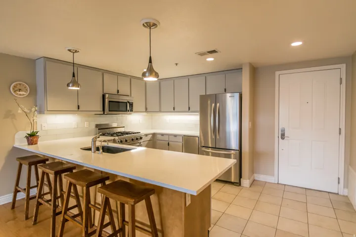 Kitchen featuring a breakfast bar, stainless steel appliances, a peninsula, decorative light fixtures, and gray cabinetry
