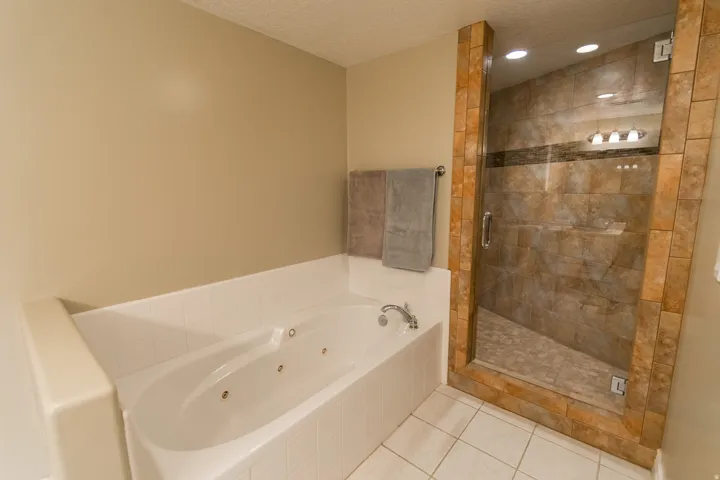 Bathroom with a jetted tub, a stall shower, light tile patterned floors, a textured ceiling, and recessed lighting