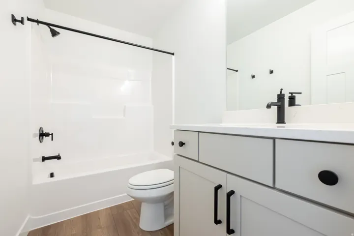 Bathroom featuring a white tub/shower combination with matte black fixtures, a white toilet, and wood-finish flooring