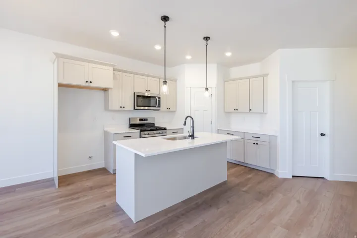 Kitchen featuring white shaker-style cabinetry, stainless steel appliances, a center island with sink, quartz countertops, and wood-finish flooring