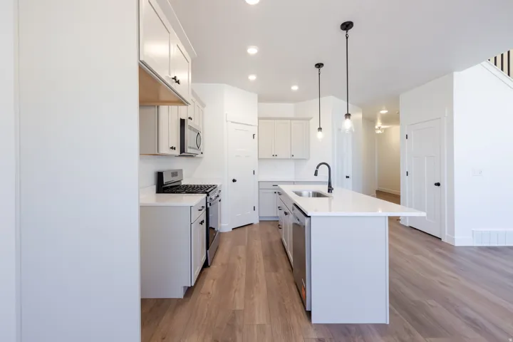 Contemporary kitchen featuring light wood-finish flooring, white cabinetry, recessed lighting, a kitchen island with pendant lighting, and stainless steel appliances