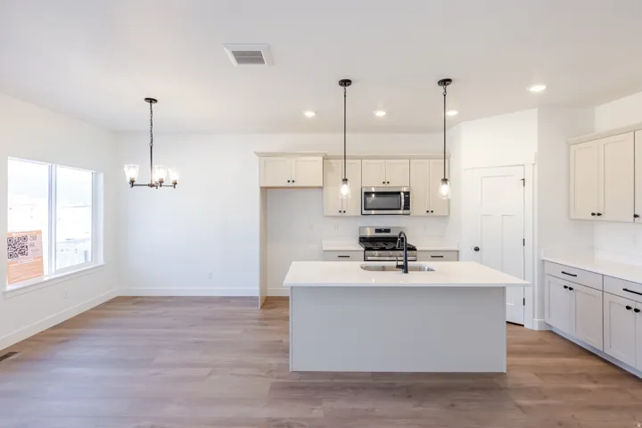 Open-concept living space featuring a central kitchen island with a matte black faucet, stainless steel appliances, light-toned cabinetry, and wood-finish flooring