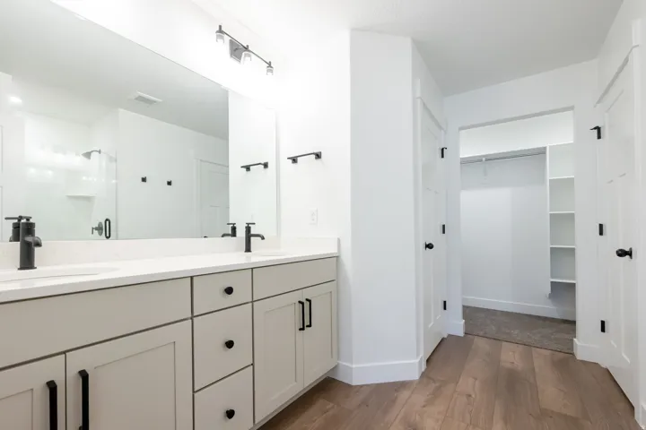 Bathroom featuring a dual vanity with light cabinetry and white countertops, matte black plumbing fixtures, and a large wall-mounted mirror
