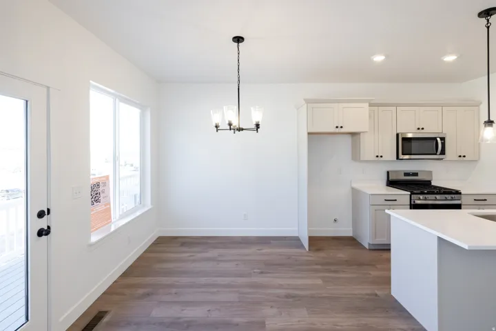 Open-concept living space featuring wood-finish flooring, a contemporary chandelier, and a large window