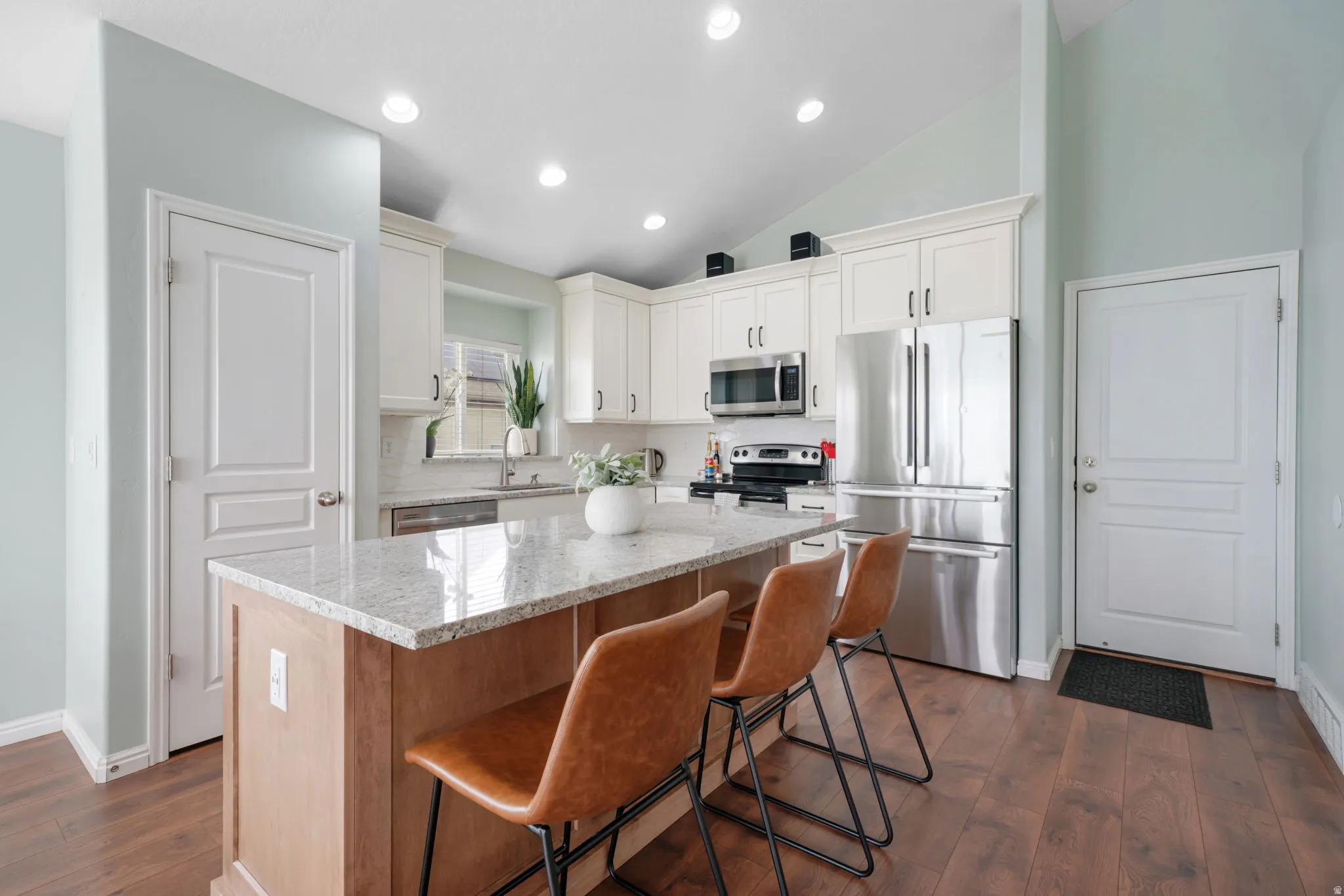 Kitchen with stainless steel appliances, light stone counters, a center island, vaulted ceiling, and a kitchen bar