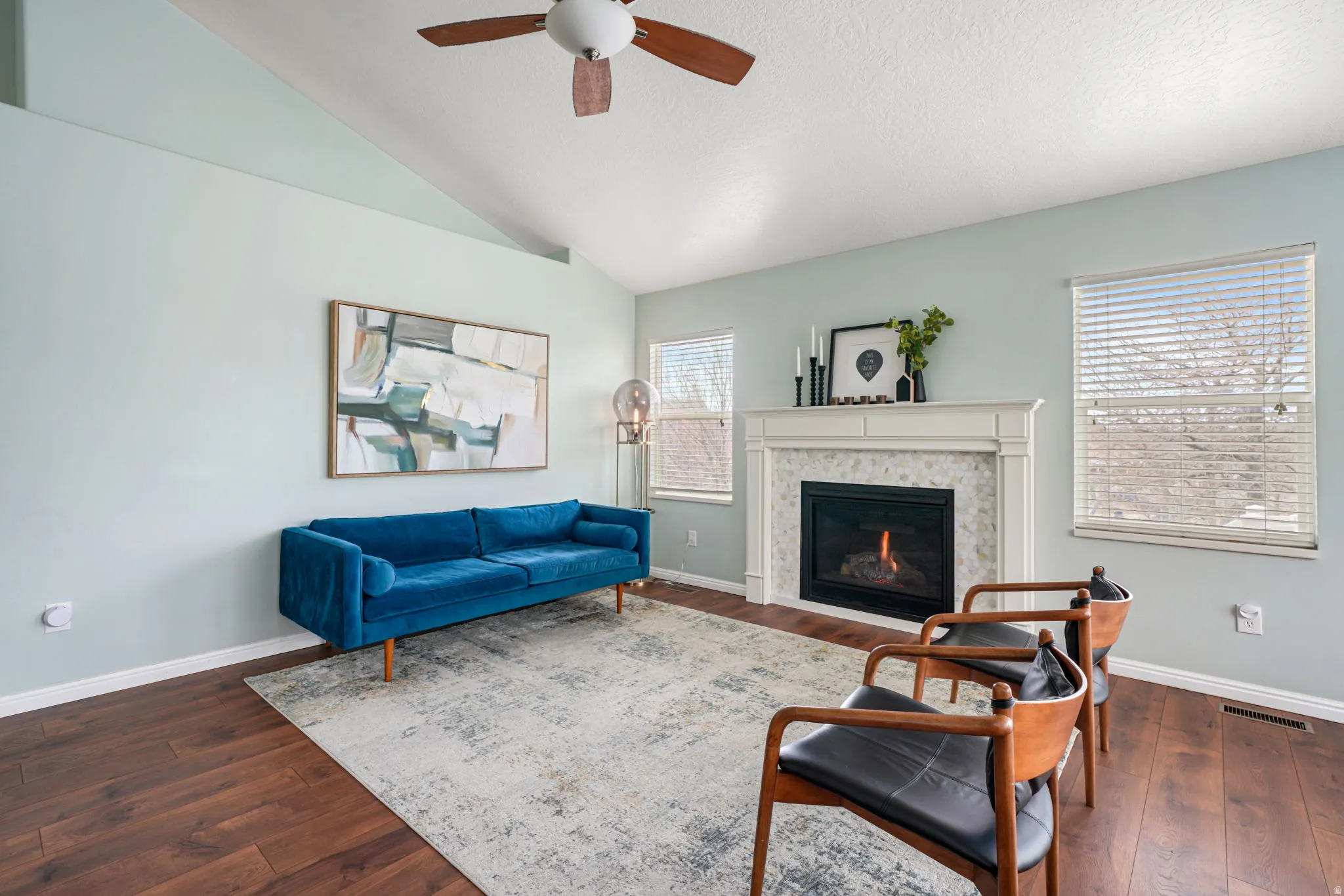 Living area featuring dark wood-type flooring, a glass covered fireplace, and ceiling fan