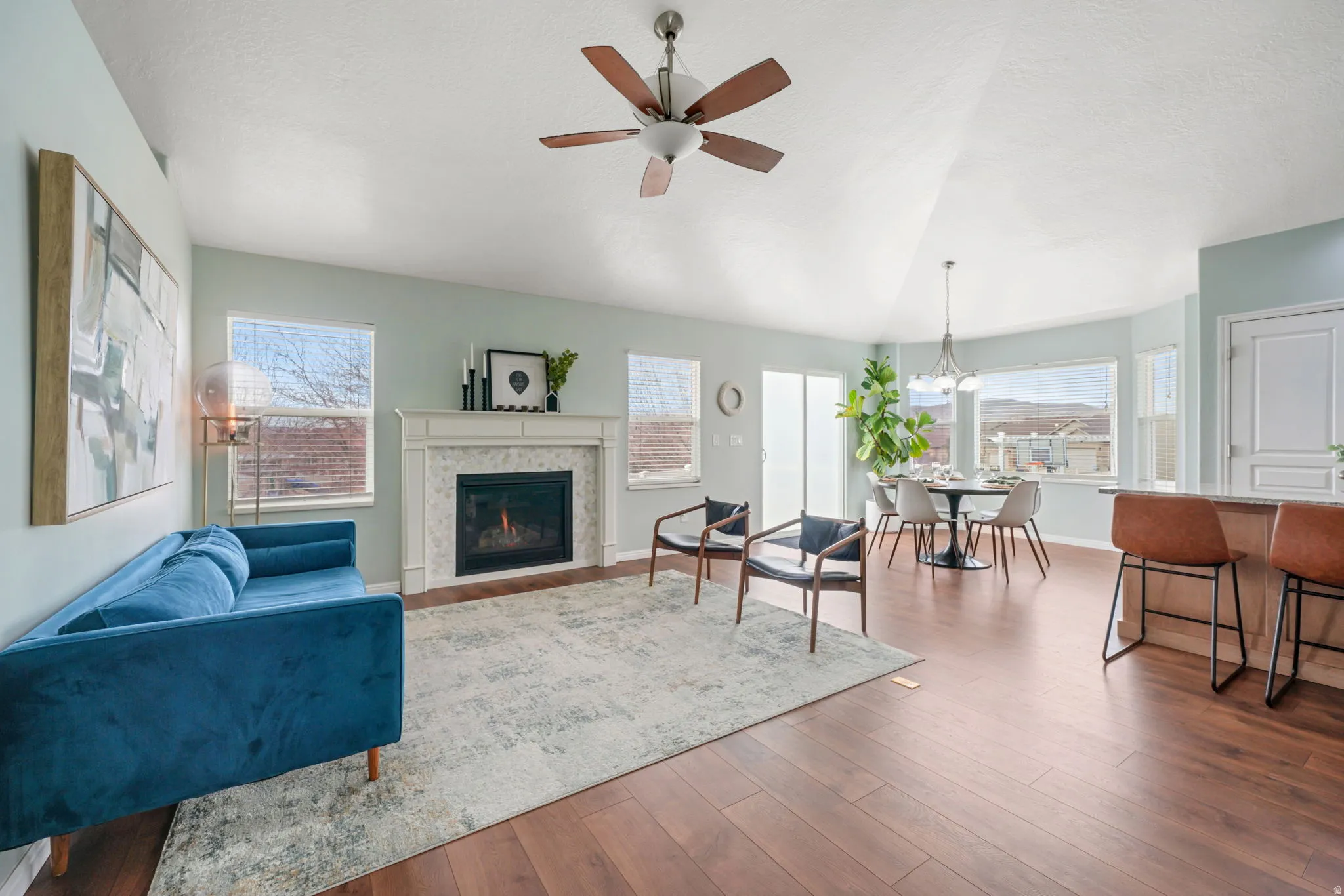 Living area with a ceiling fan, dark wood-type flooring, plenty of natural light, and a tile fireplace