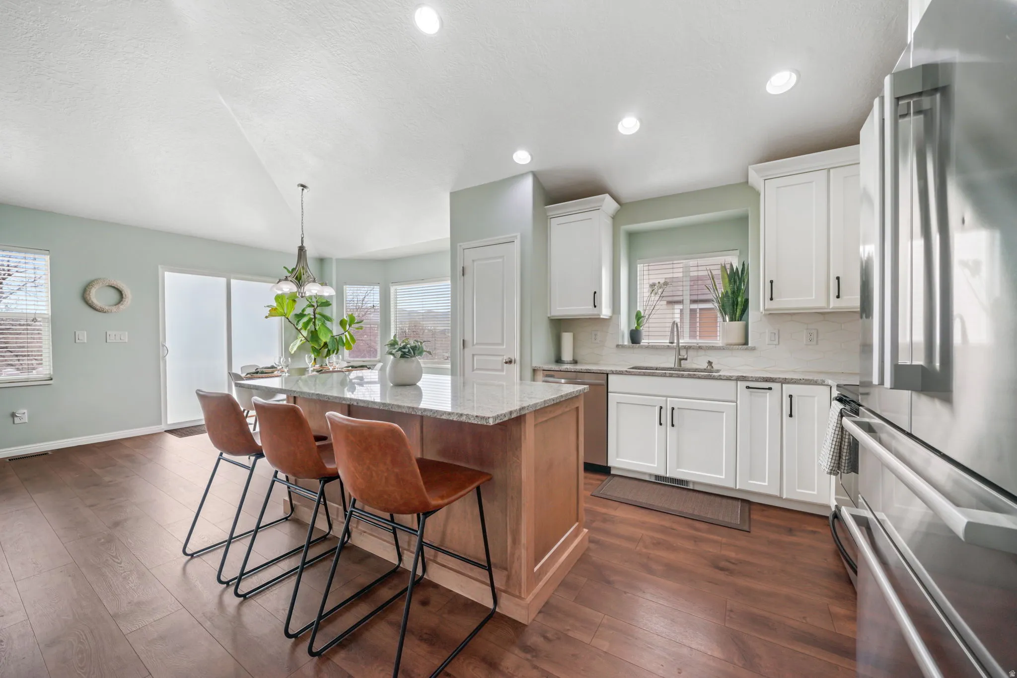 Kitchen featuring stainless steel appliances, light stone countertops, two tone cabinetry, a center island, and dark wood finished floors