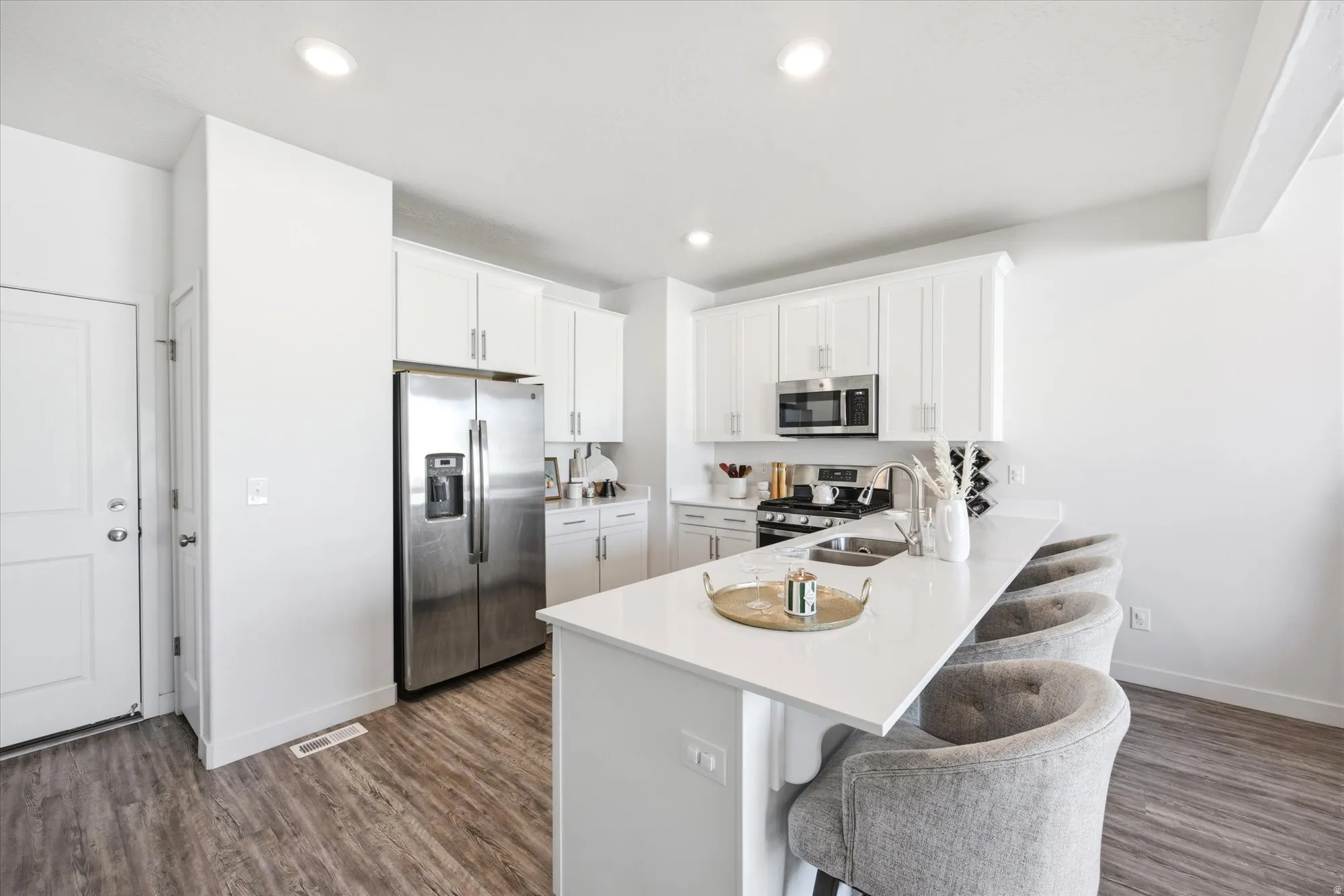Kitchen with stainless steel appliances, a peninsula, white cabinetry, a breakfast bar, and dark wood finished floors