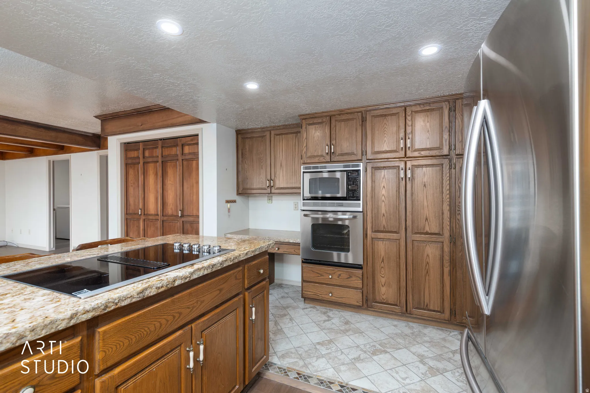 Kitchen featuring stainless steel appliances, wood finish cabinets, a textured ceiling, light stone counters, and recessed lighting